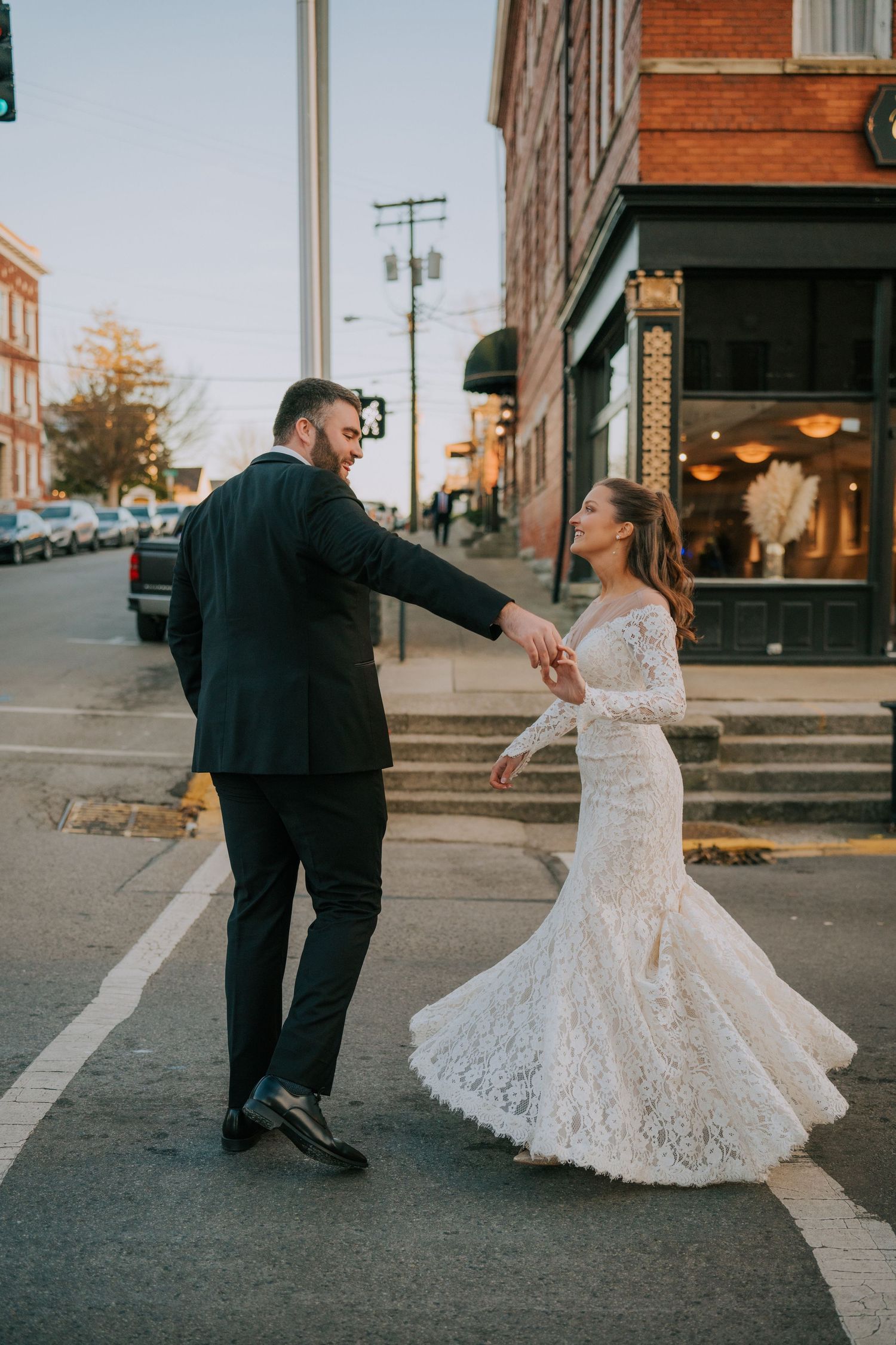 A newlywed couple dances together on a charming urban street corner at dusk.