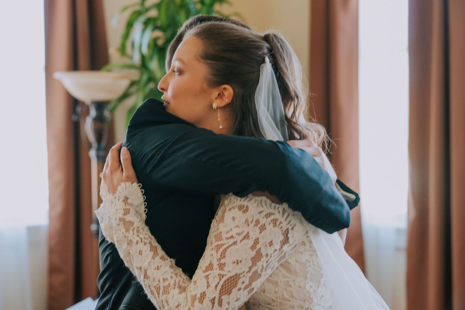 Emotional embrace between a bride in a lace wedding dress and someone in a dark suit at a wedding.