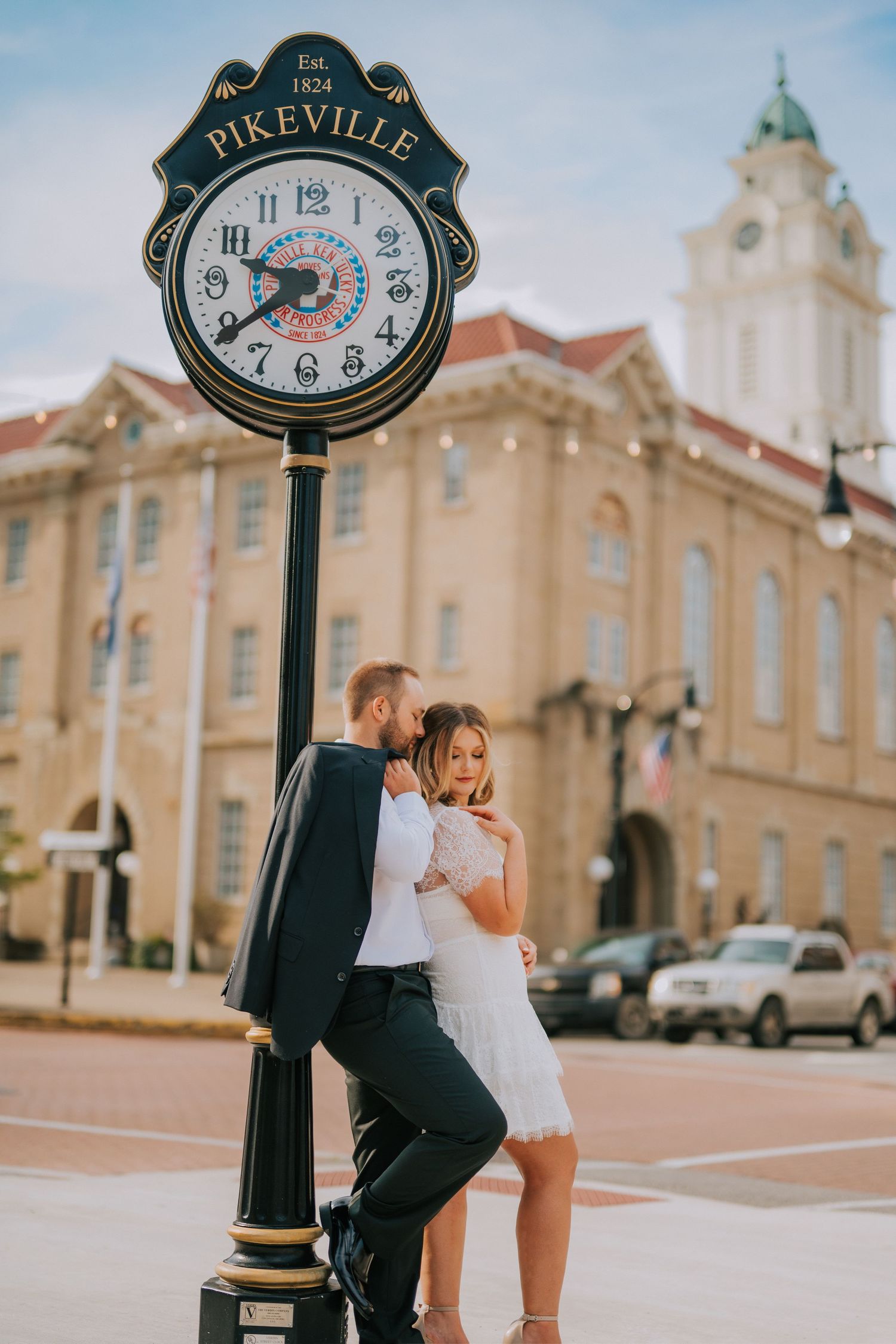 A couple poses near a vintage clock in front of a historic courthouse building in Pikeville.