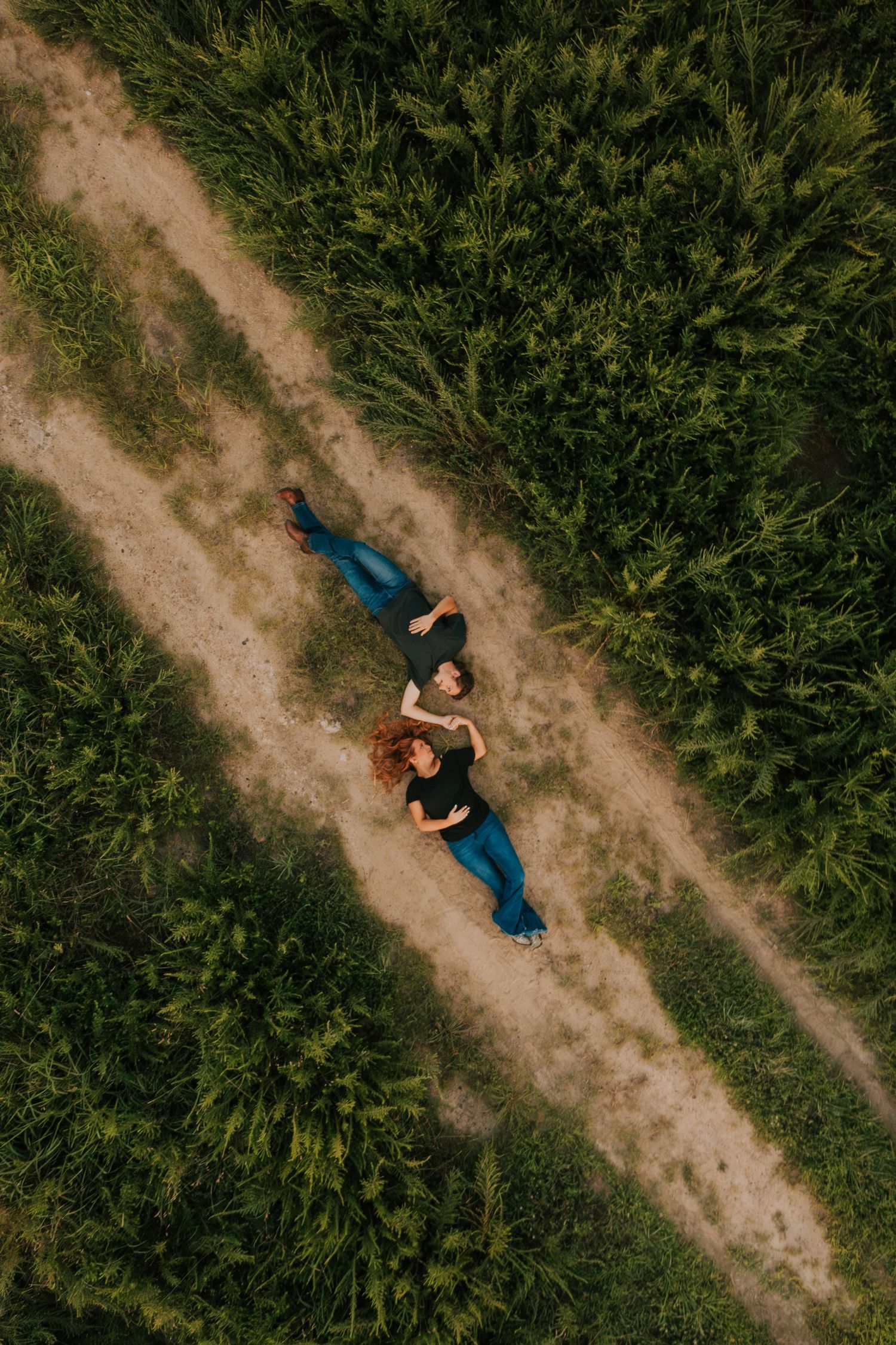 Aerial view of two people lying on a dirt path surrounded by green vegetation.