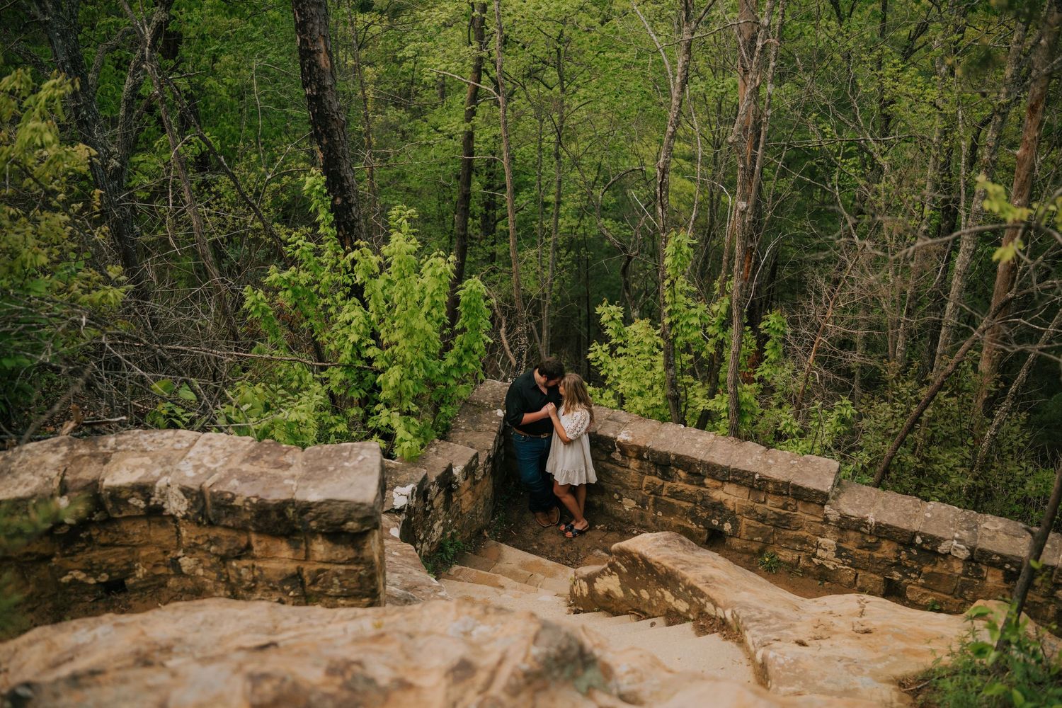 Romantic outdoor photo session on stone overlook surrounded by forest scenery.