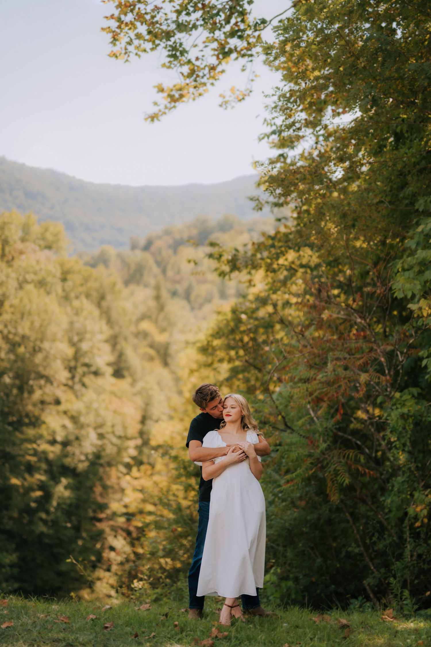 Romantic scene with couple embracing against backdrop of mountain forest in golden light.