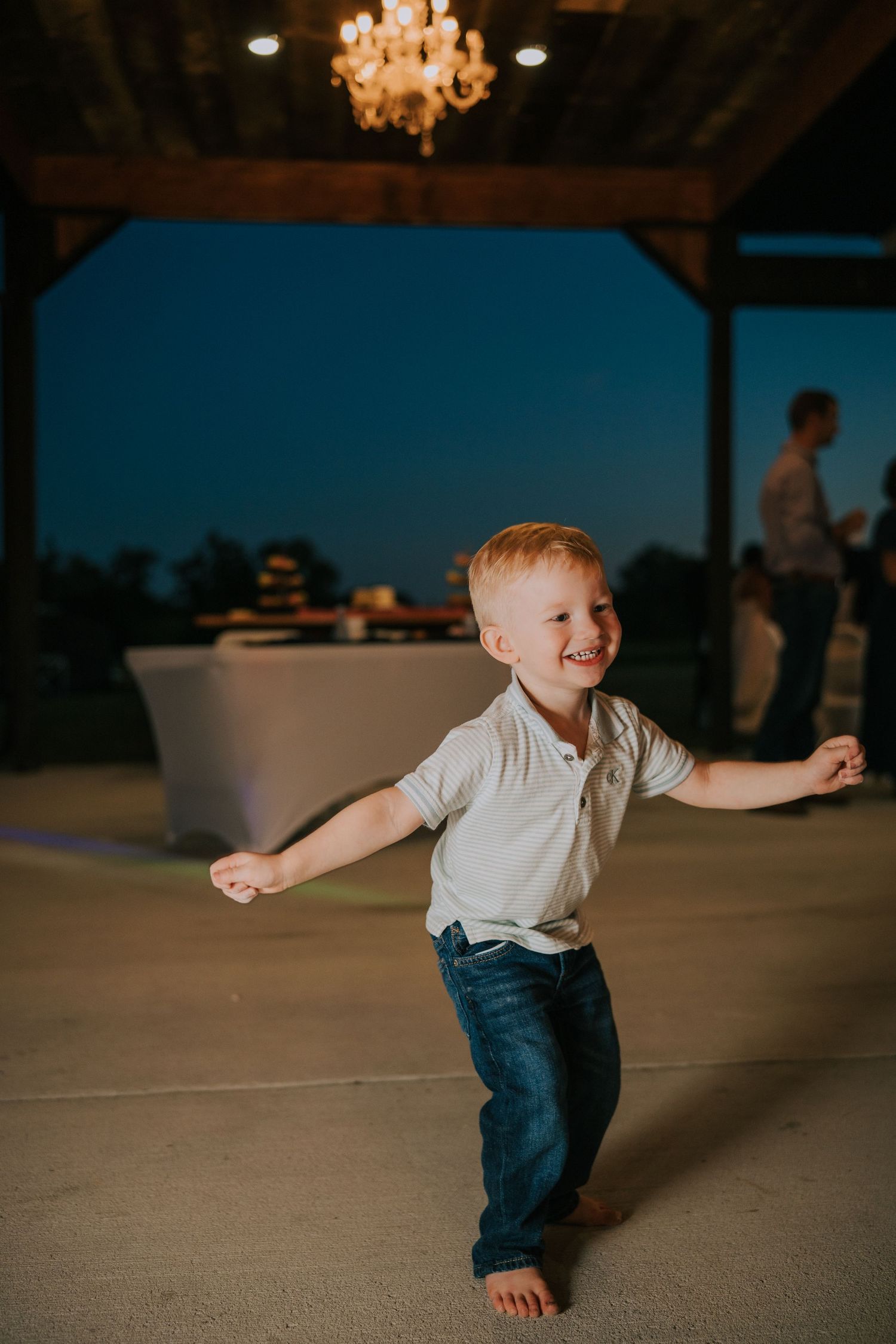 Young child dancing and spinning on reception dance floor under chandelier lighting.