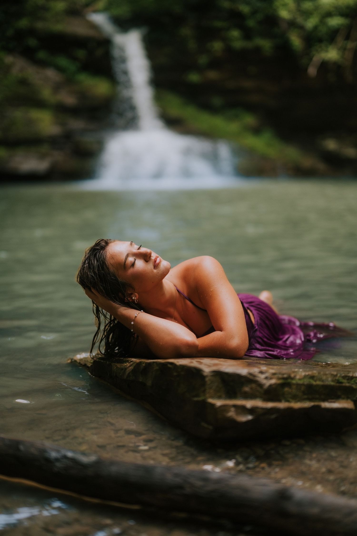 A serene waterfall scene with someone reclining on a rock in purple clothing.