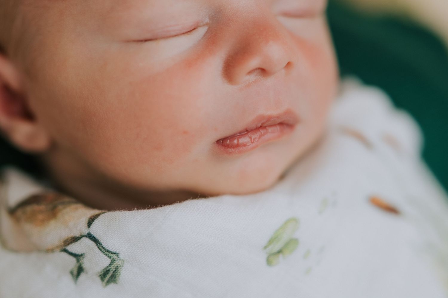 Newborn baby wearing soft mint green outfit lying on beige textured blanket.