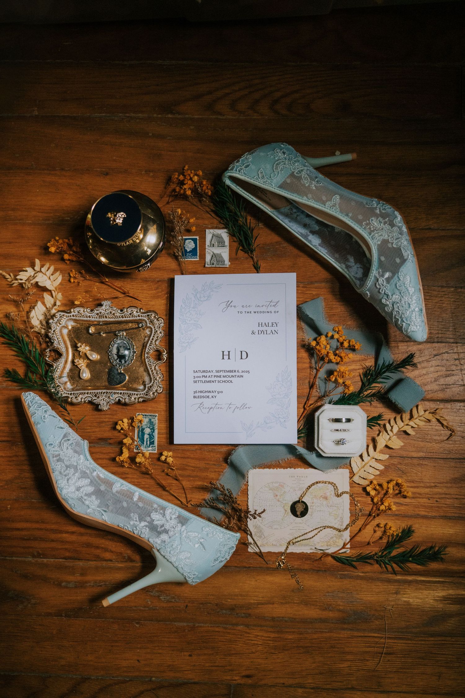 Wedding accessories including blue heels, invitation and jewelry arranged on a dark wooden surface.