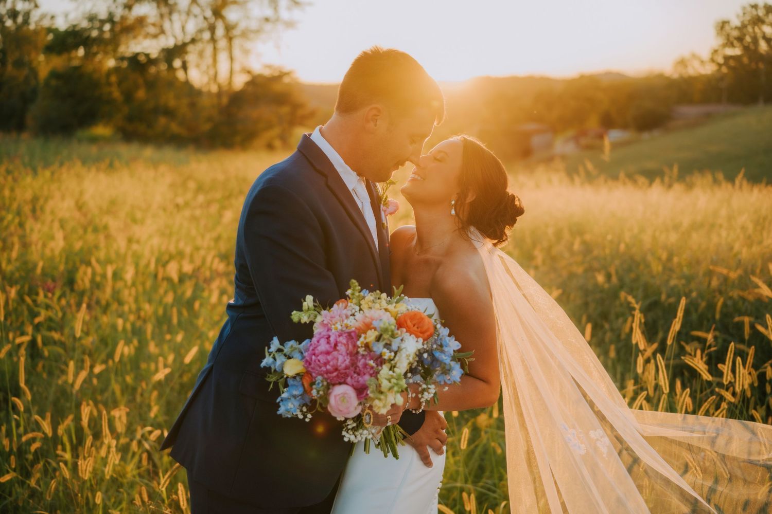 Golden hour wedding photography with sunflare and flowing veil in a meadow.