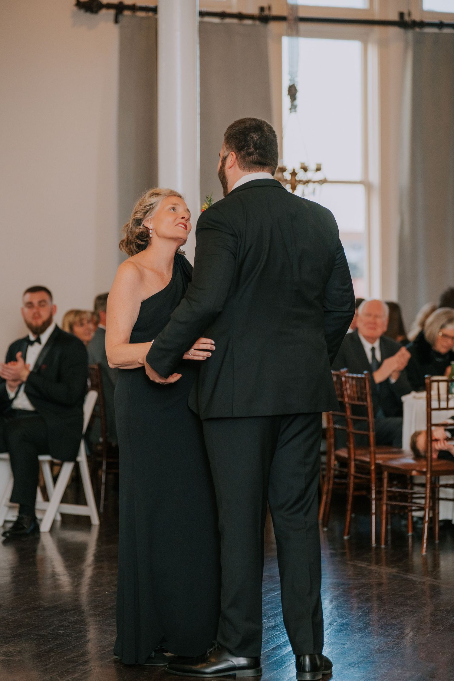 Couple dancing together at formal event with guests seated in background watching.