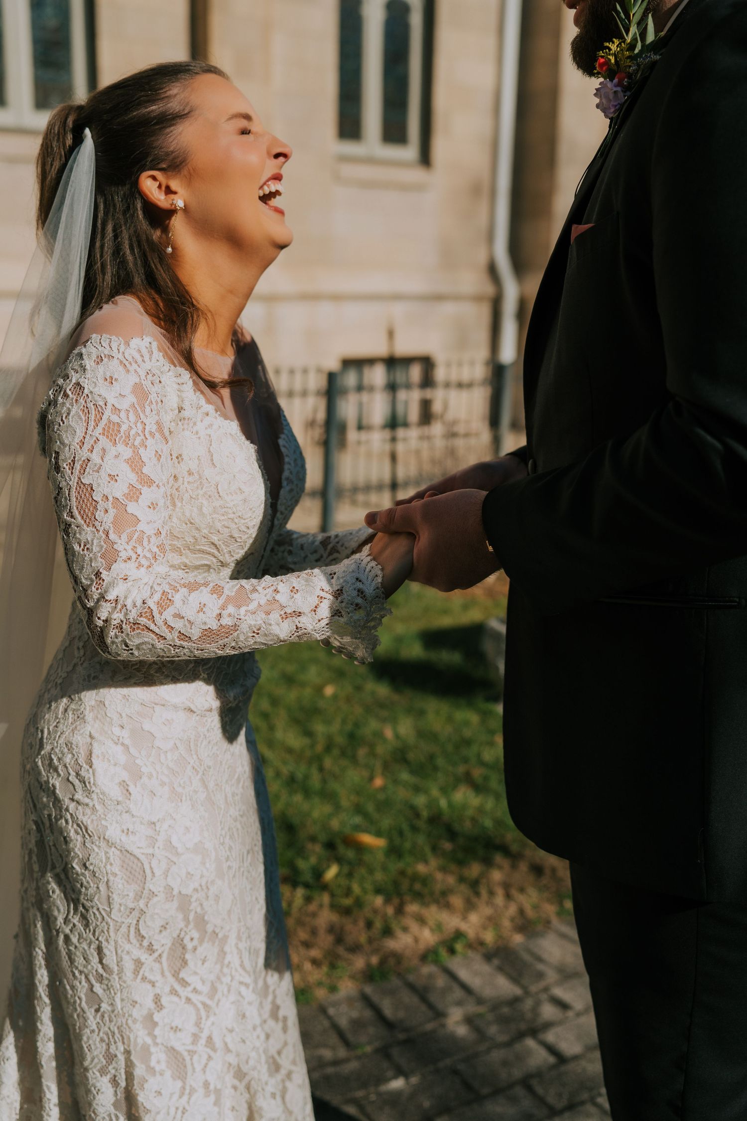 A joyful moment during a wedding ceremony as a bride in a long-sleeved lace gown laughs outdoors.