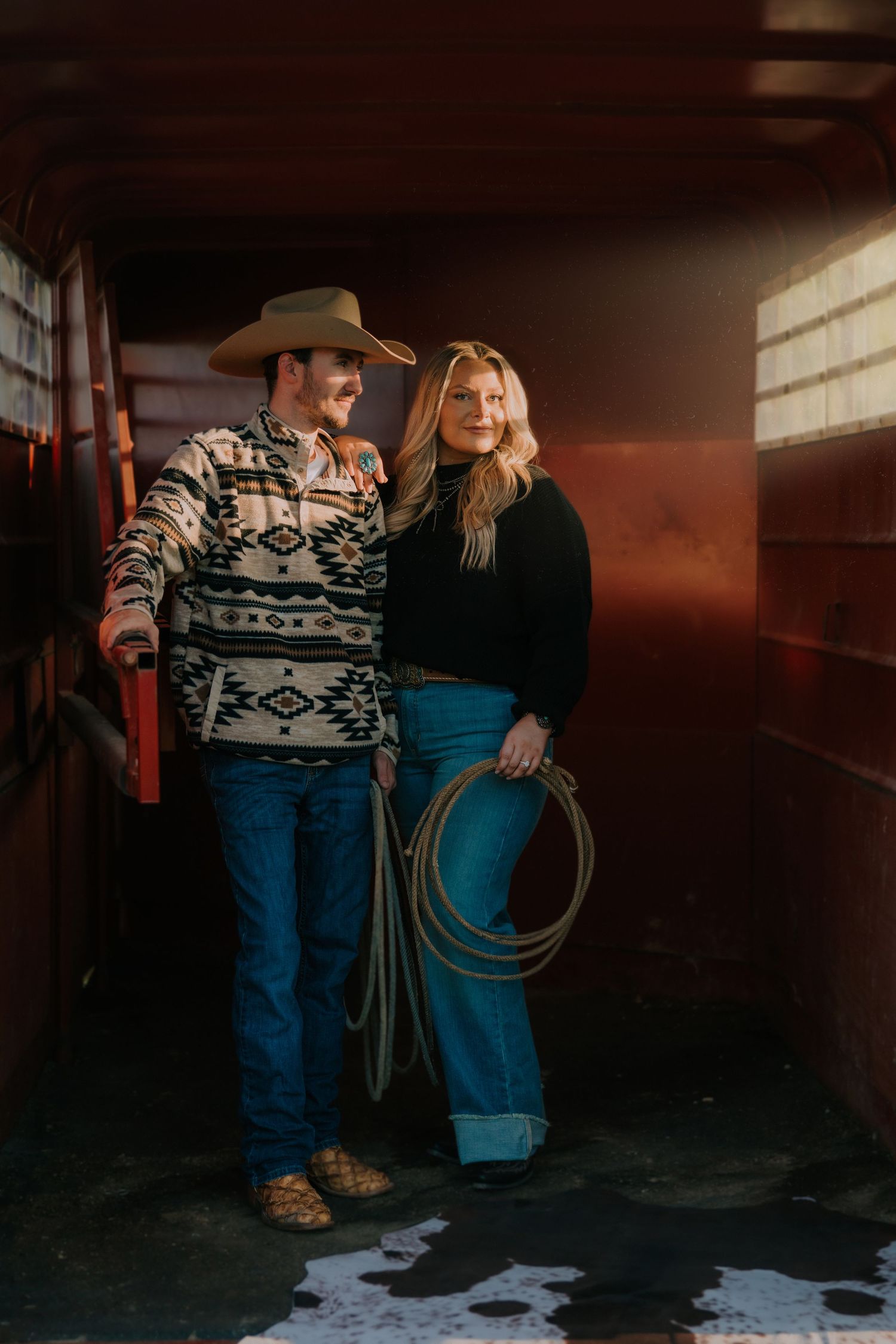 Western-styled couple in rustic barn setting with rope and geometric pattern sweater.