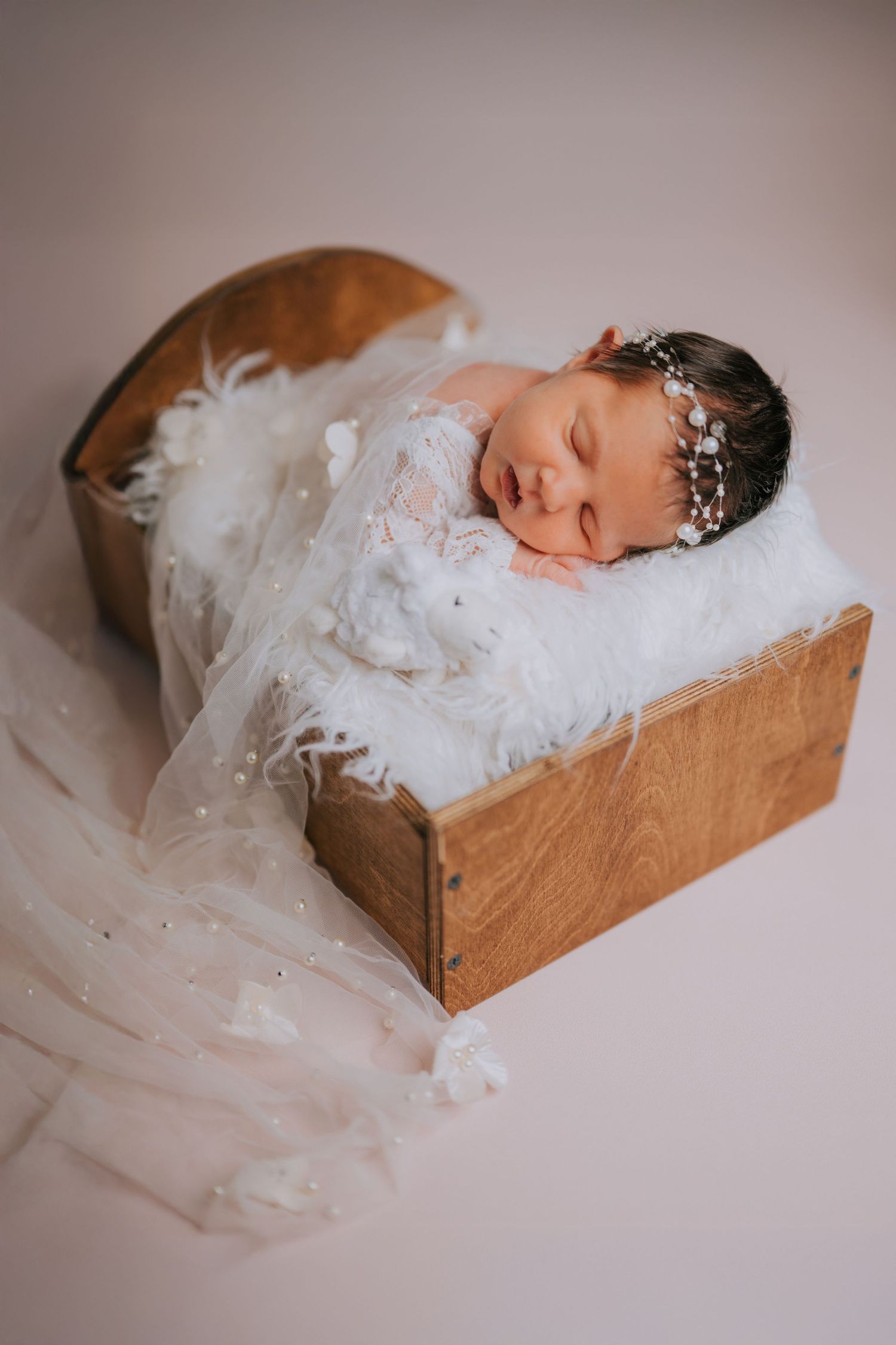 Newborn sleeping in wooden box surrounded by delicate white tulle fabric.