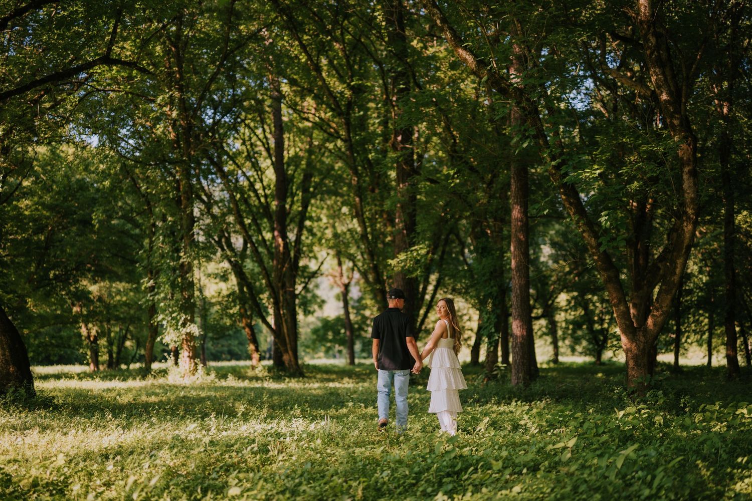 A couple embraces in a lush green forest setting during a romantic photoshoot.