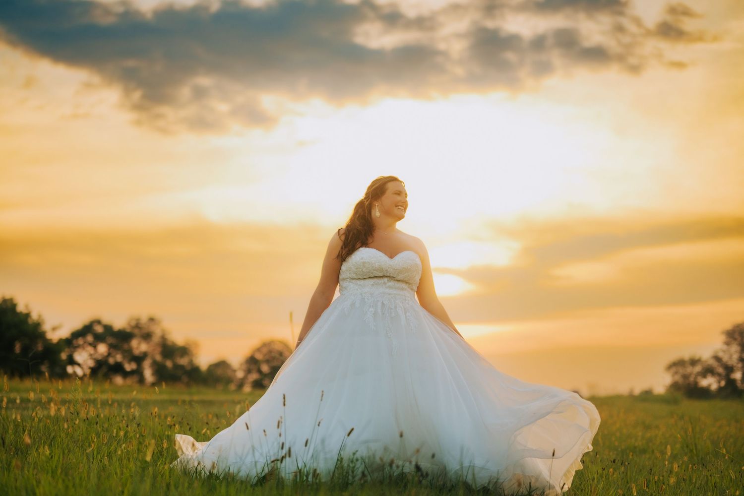 A white wedding dress flows in a golden sunset field creating a dreamy silhouette.