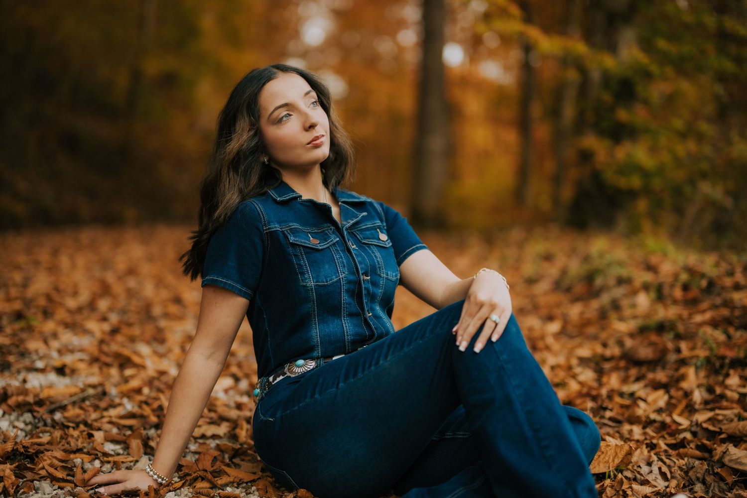 Person in denim lounging on autumn leaves during an outdoor photoshoot.