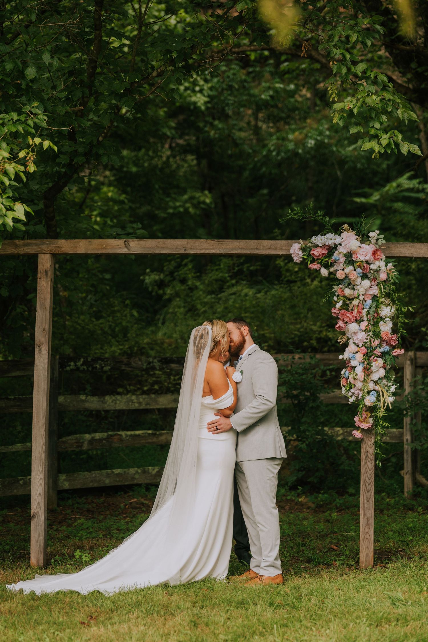 Romantic wedding ceremony setup with floral arch and wooden fence in a lush garden setting.