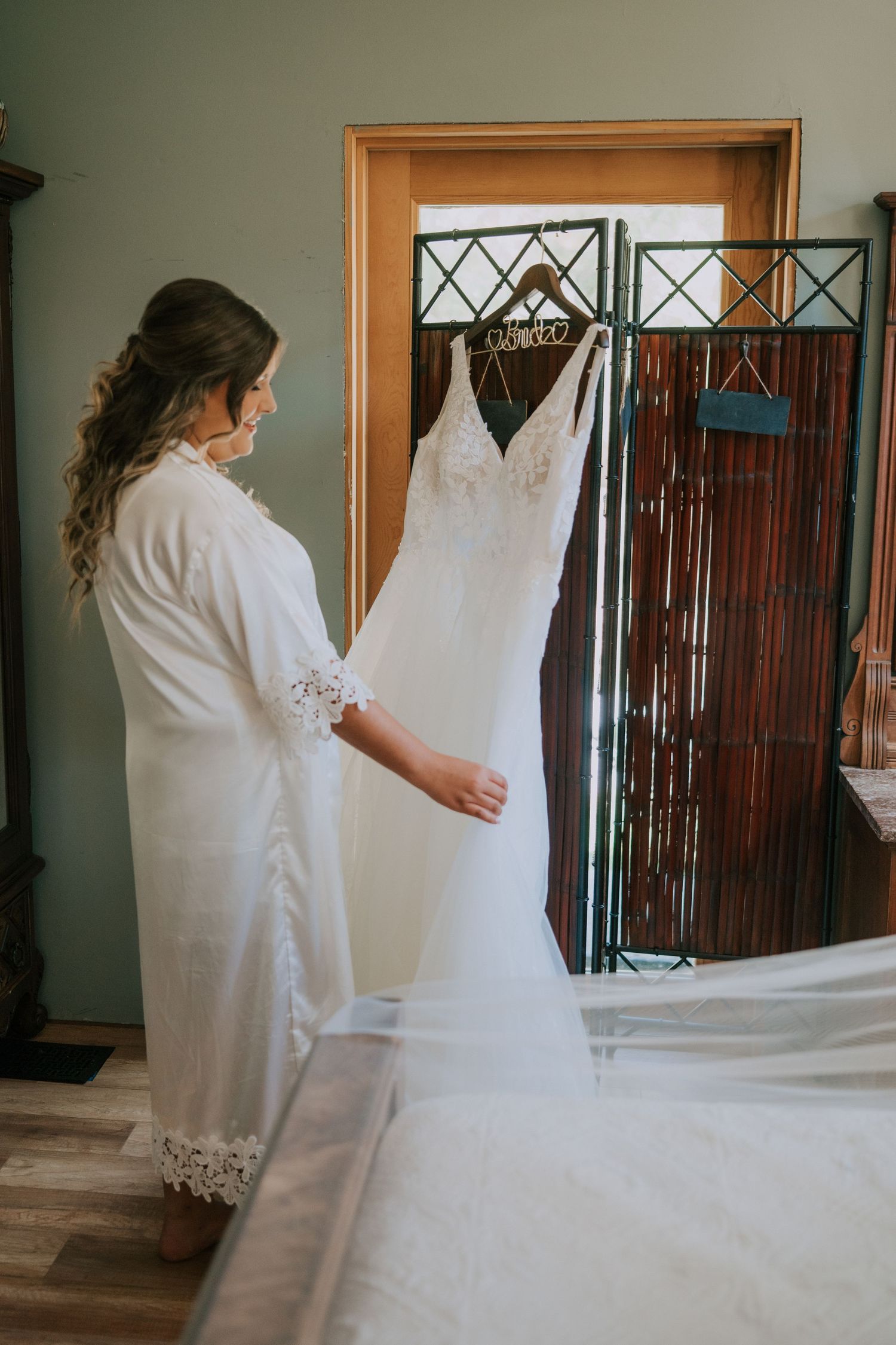 A person in a white robe admires a hanging wedding dress in a dressing room.