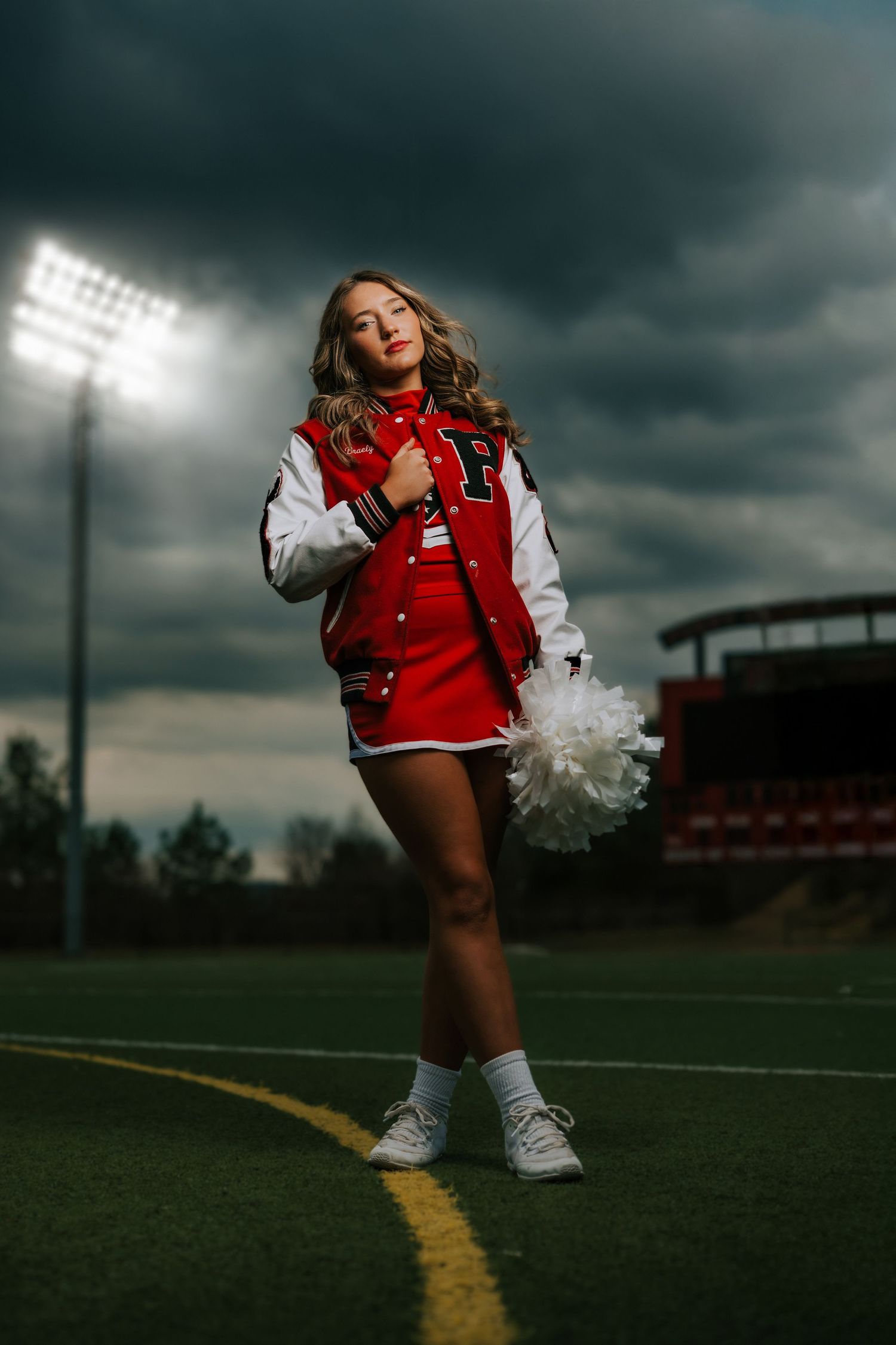 Cheerleader in red and white uniform performs dynamic poses against dramatic stormy sky at sports field.