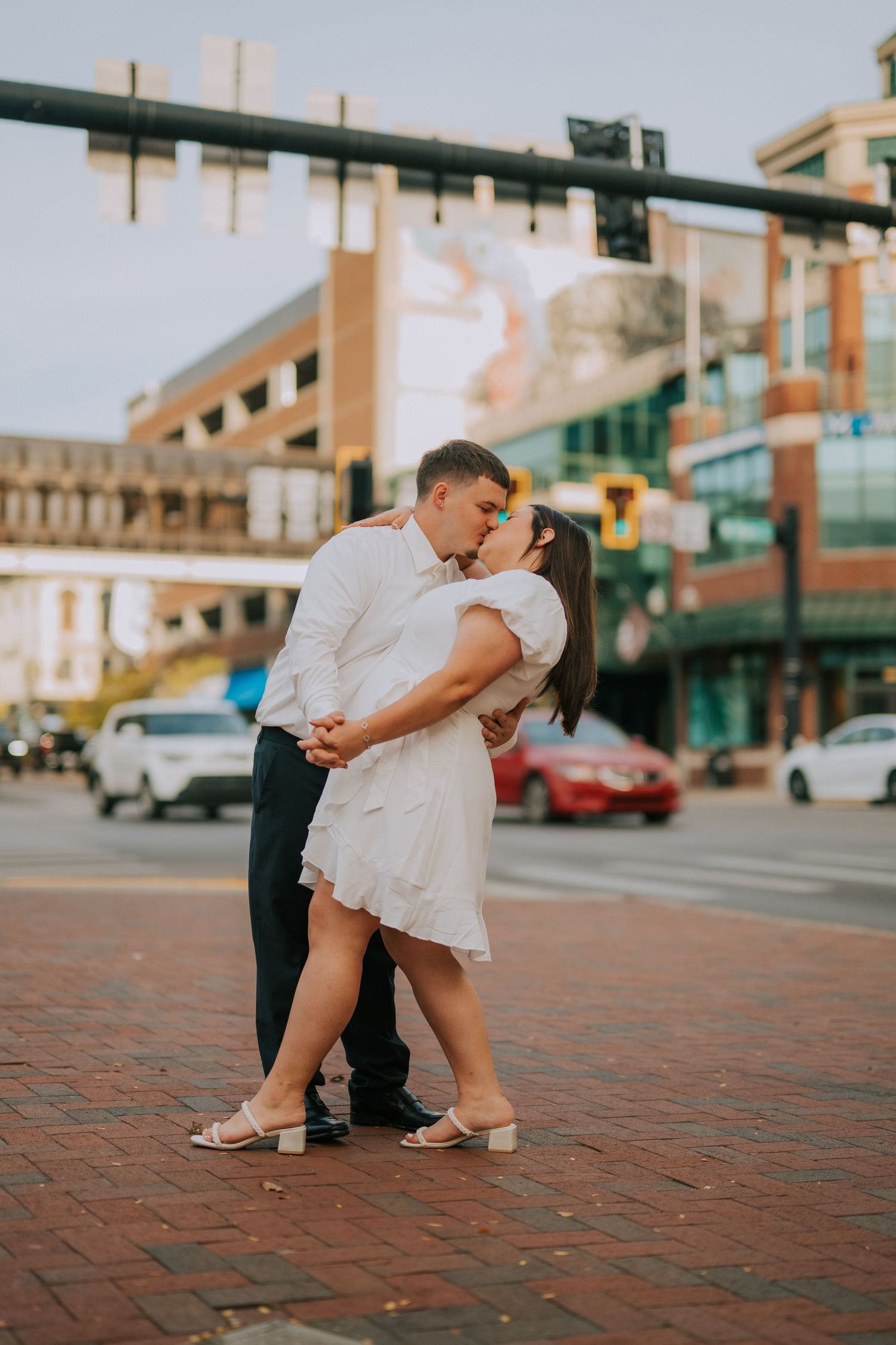 A romantic photoshoot on brick pavement with urban buildings in the background.