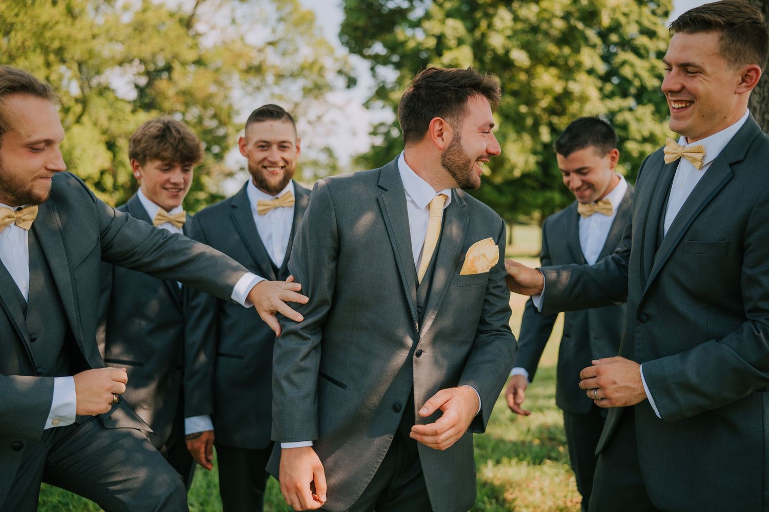 Groomsmen in dark suits share a candid laughing moment outdoors.