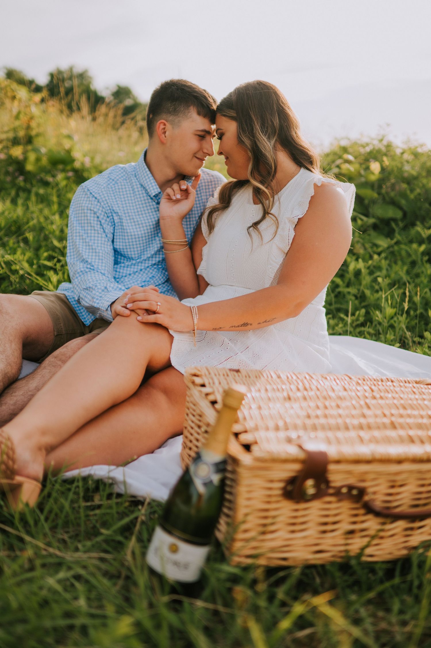A couple shares intimate moments near a picnic basket in a grassy field.