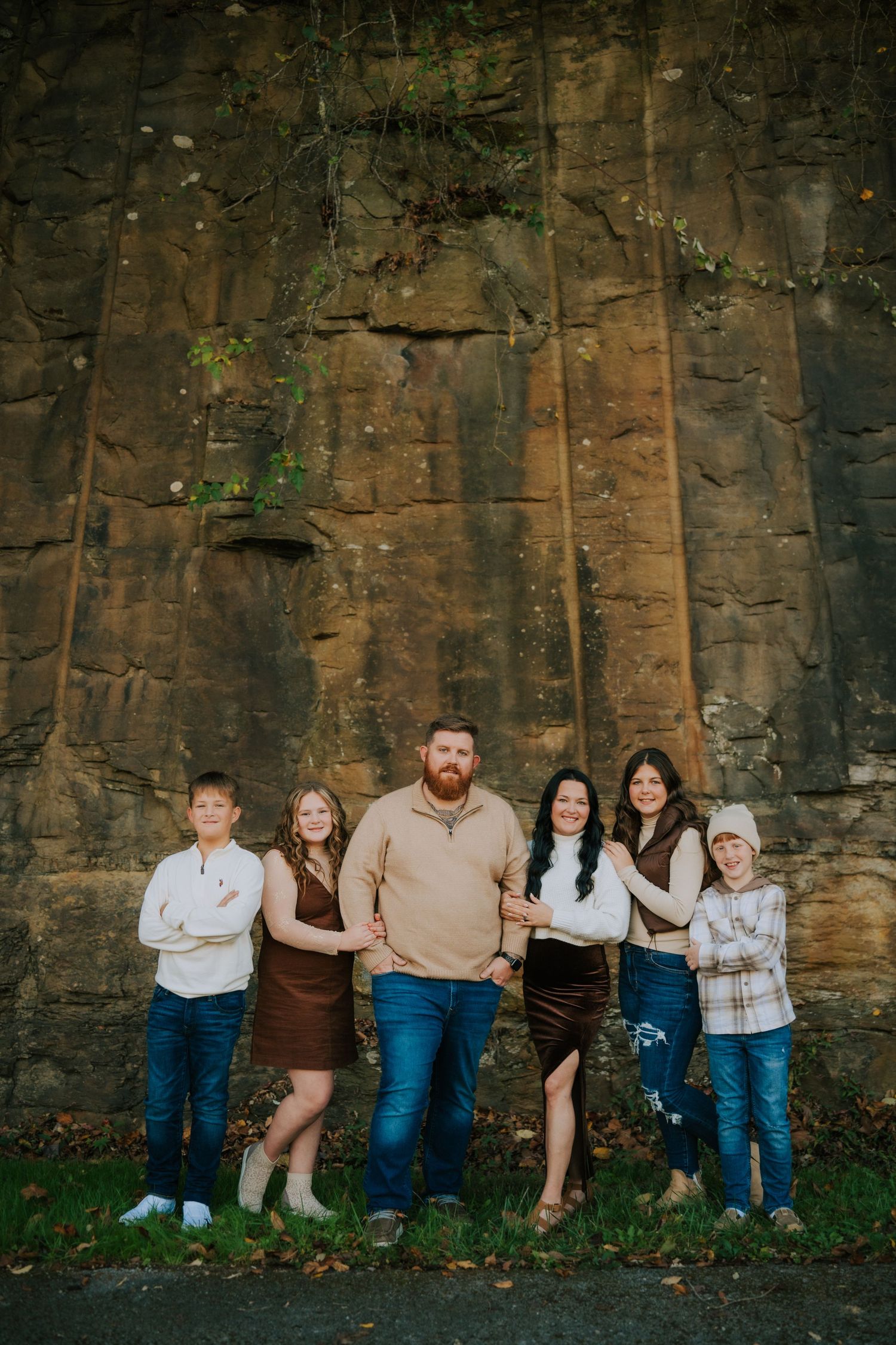 Family group poses against textured stone wall during outdoor photo session.