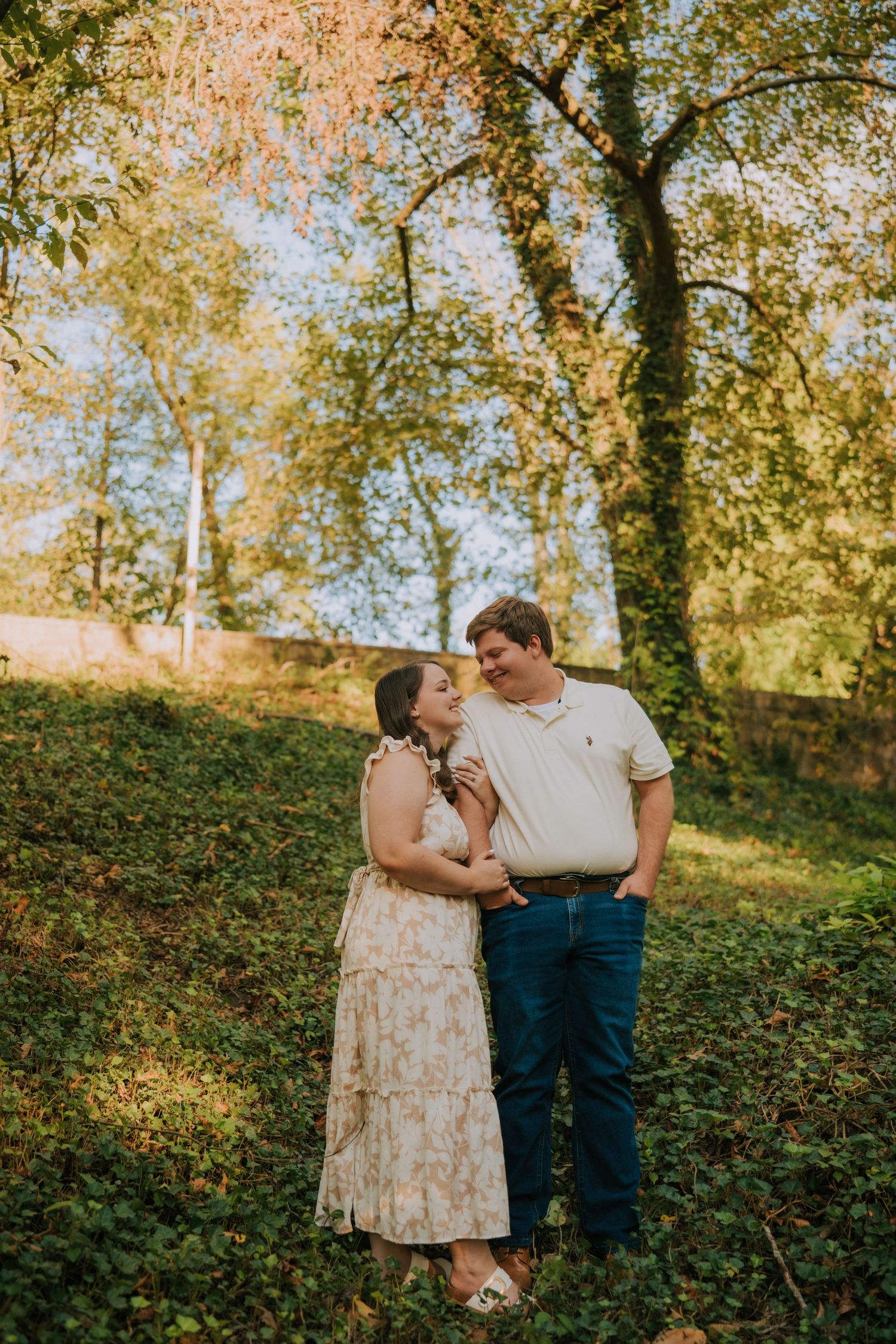 A romantic couple's portrait session on a grassy hillside with trees in the background.