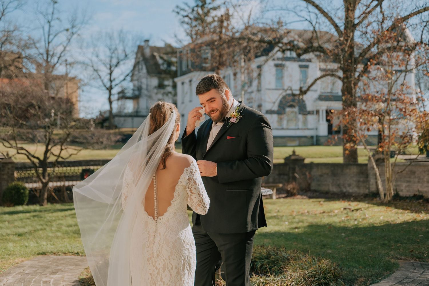 A romantic wedding couple shares a moment in front of a stately mansion on a sunny autumn day.
