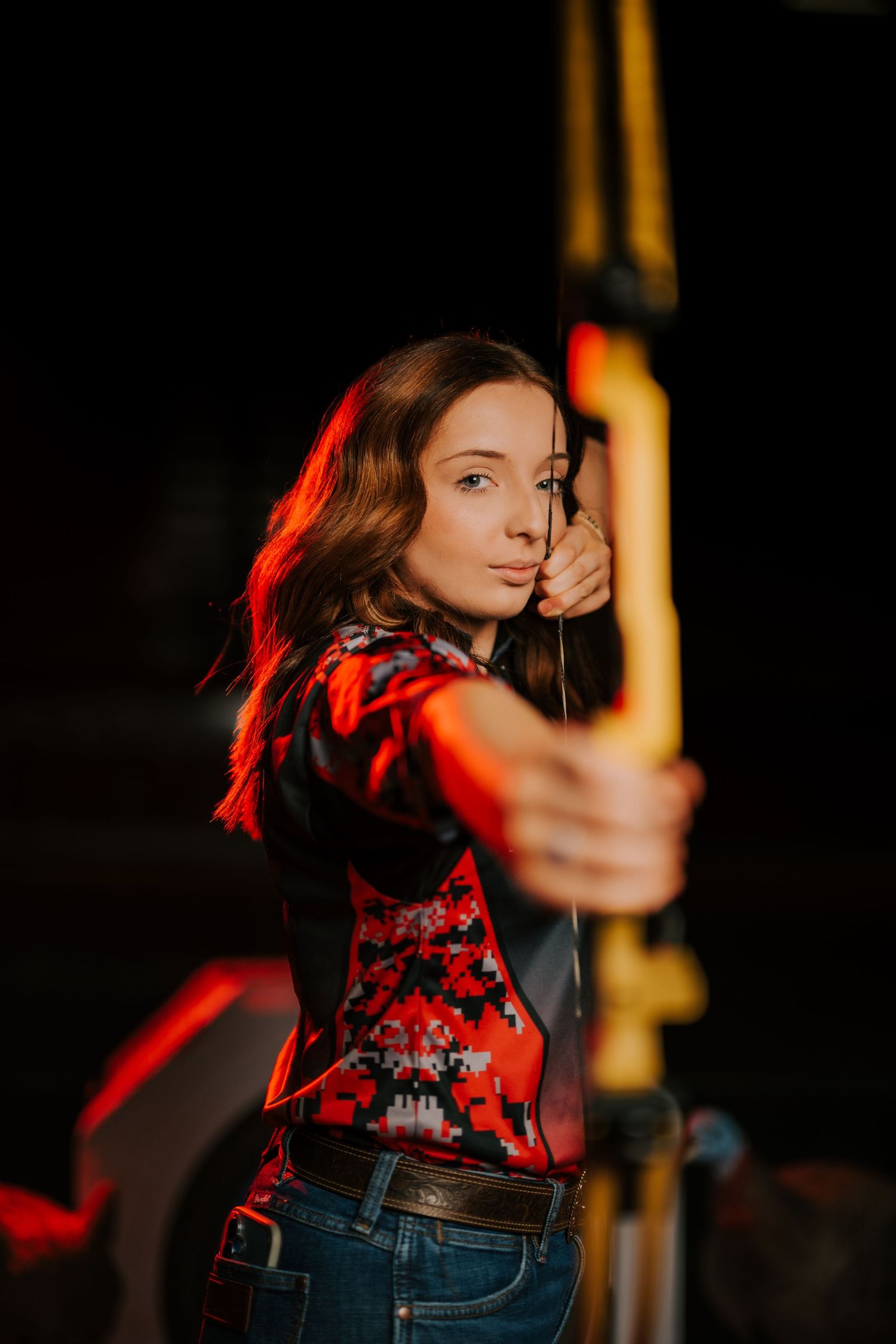 A person in a red floral top and jeans dances expressively against a dark background with dramatic lighting.