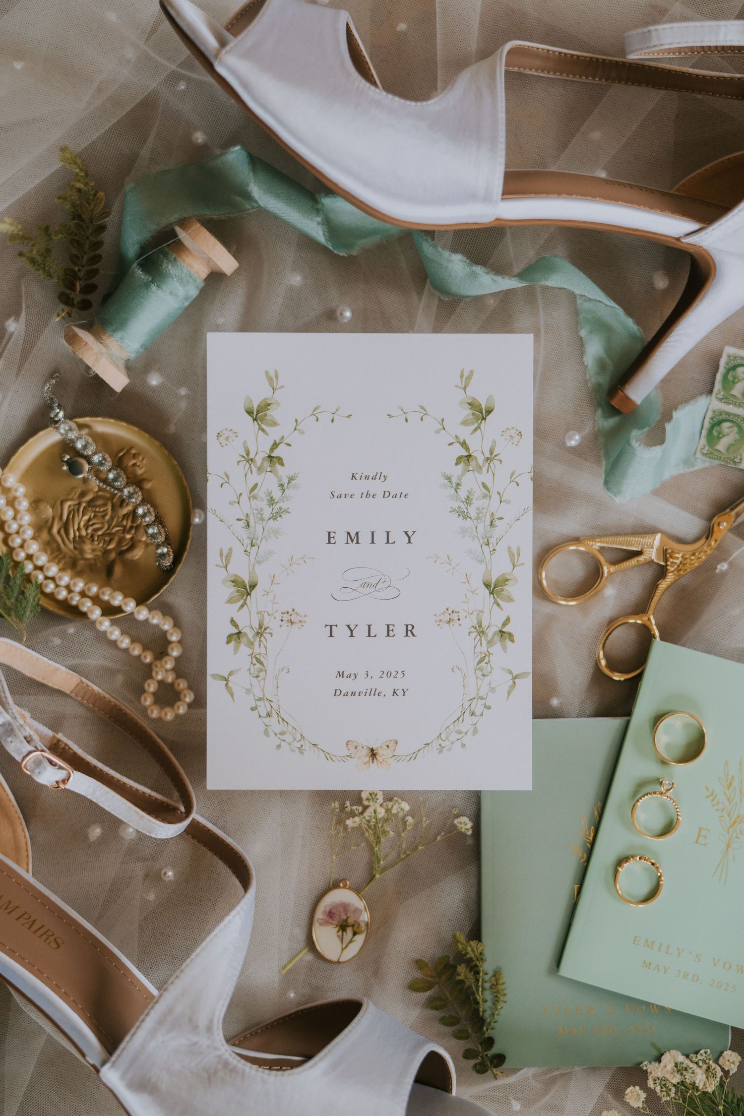 Wedding details flatlay with mint green invitations, pearl jewelry, and gold rings on a neutral background.