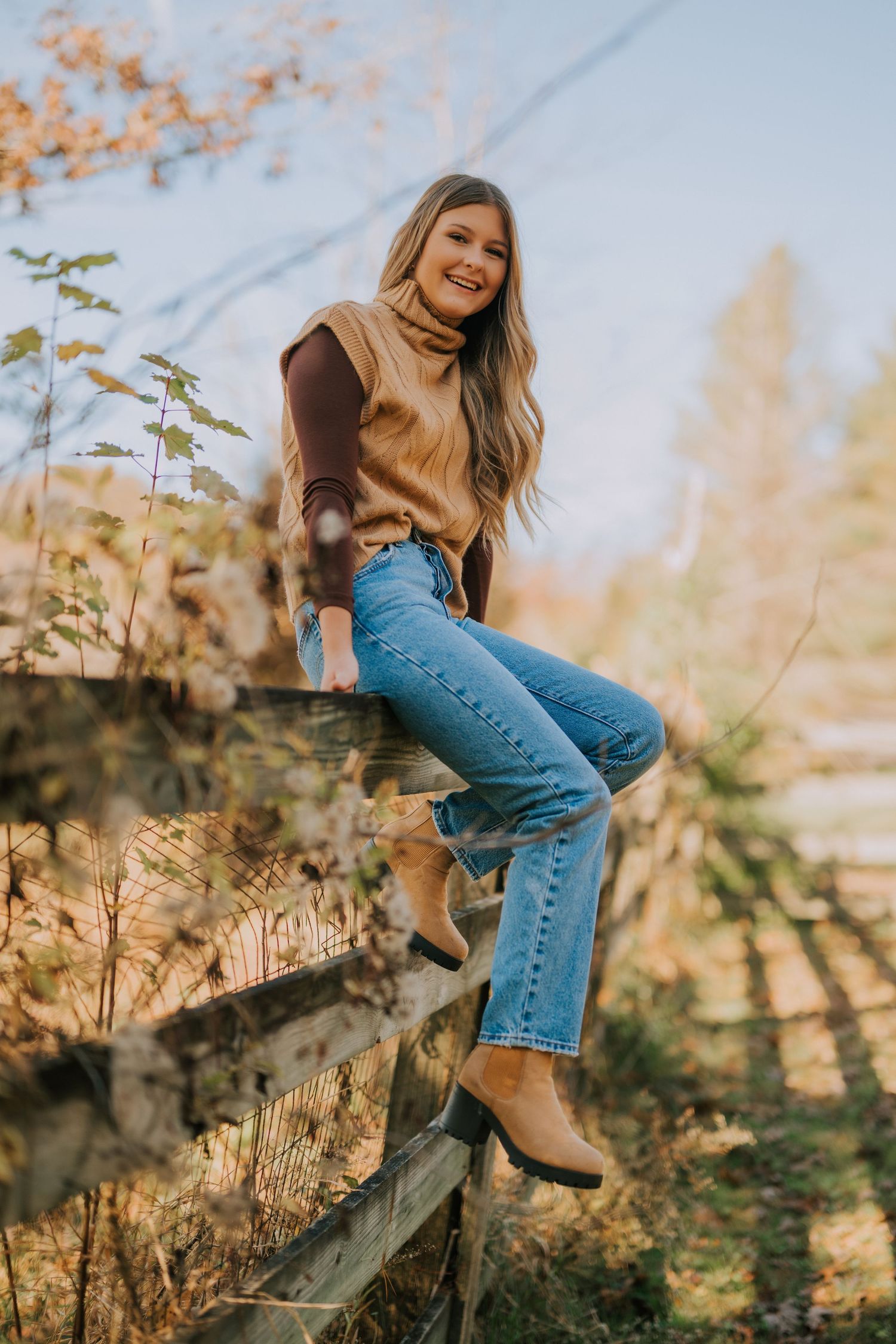 Casual portrait session by wooden fence during fall with warm sunset lighting.