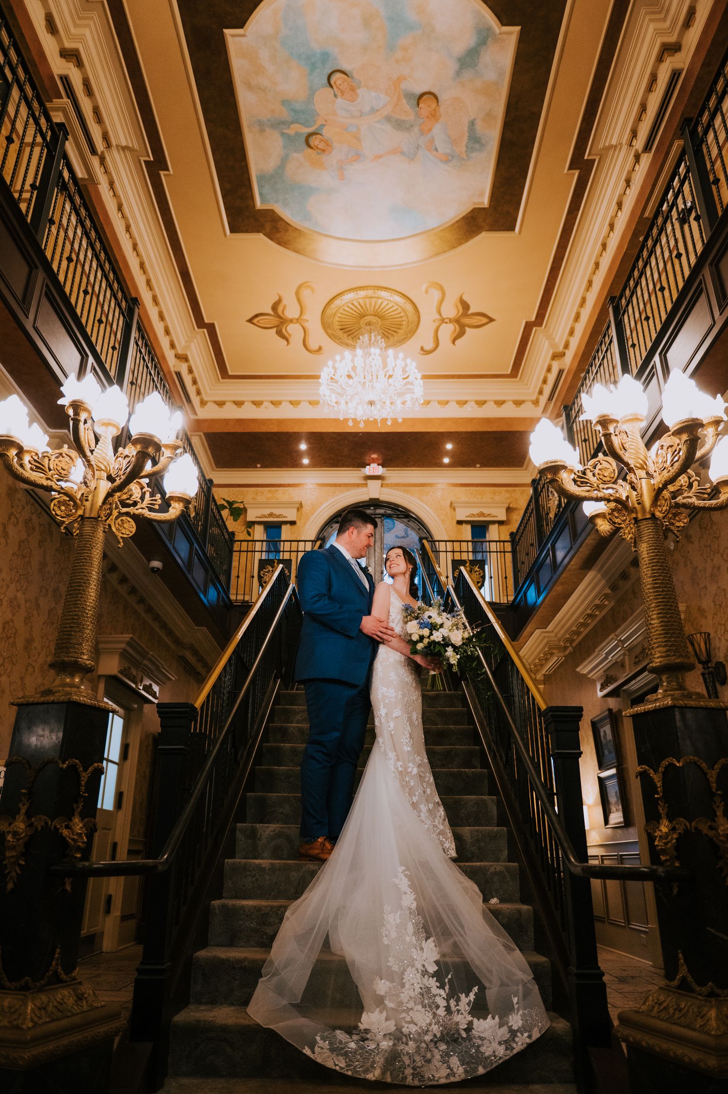 Elegant ballroom wedding scene with ornate ceiling and chandelier lighting.