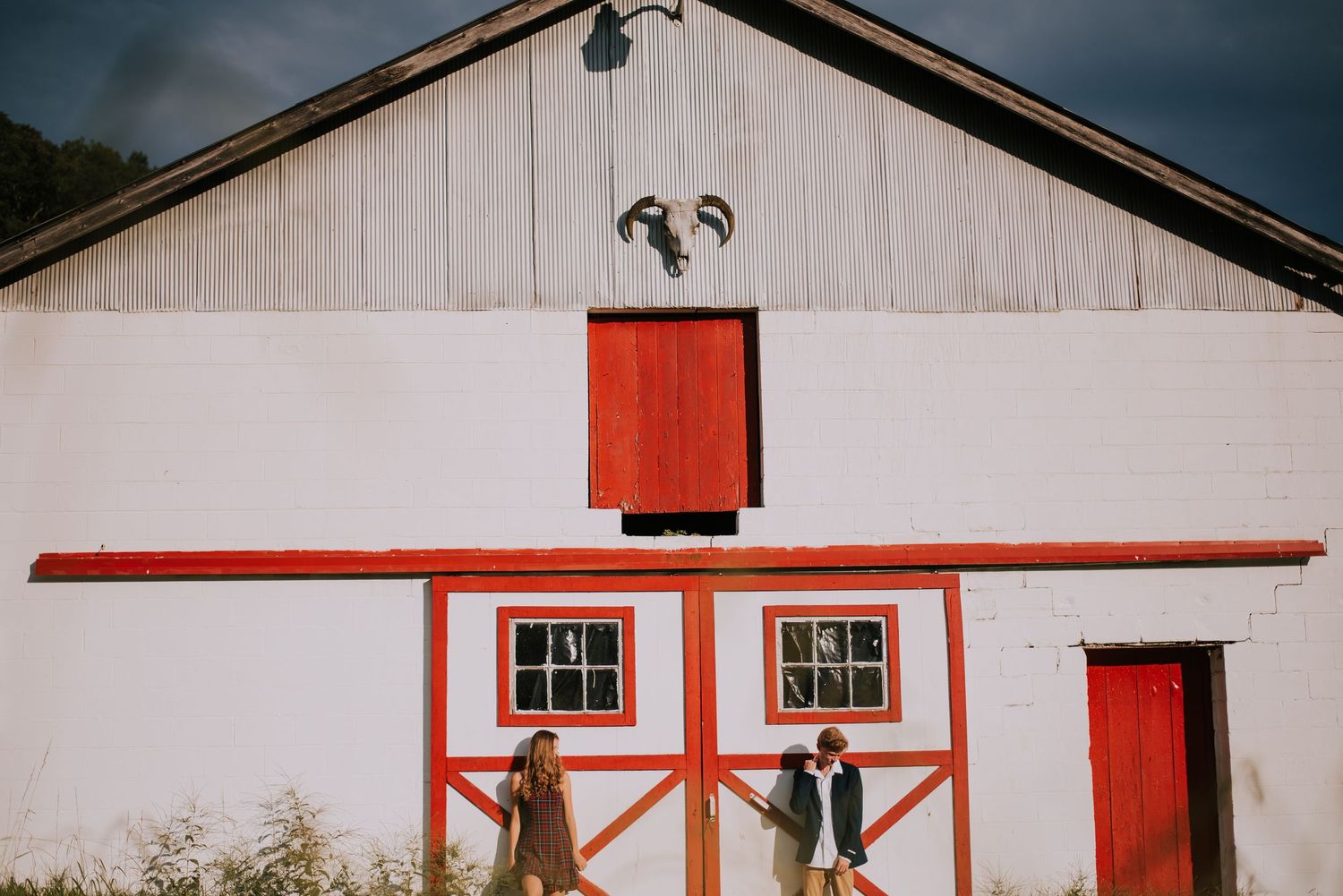 White barn with red trim photographed under moody sky conditions.