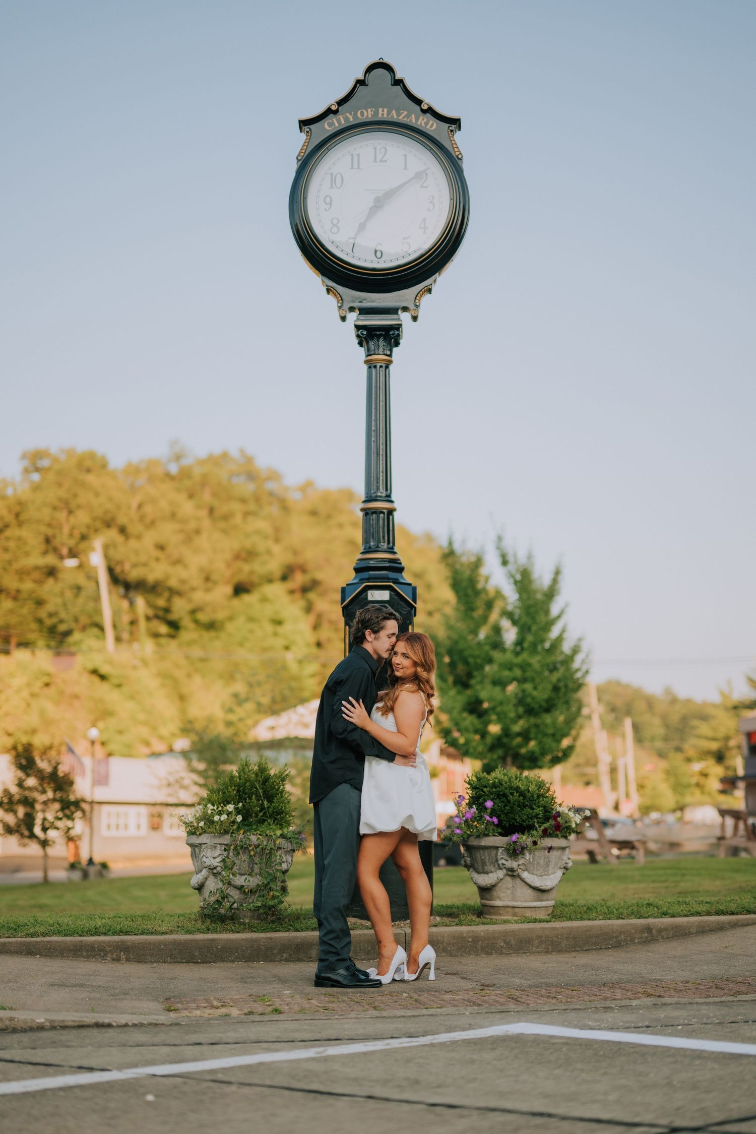 A decorative street clock stands in a park setting during golden hour.