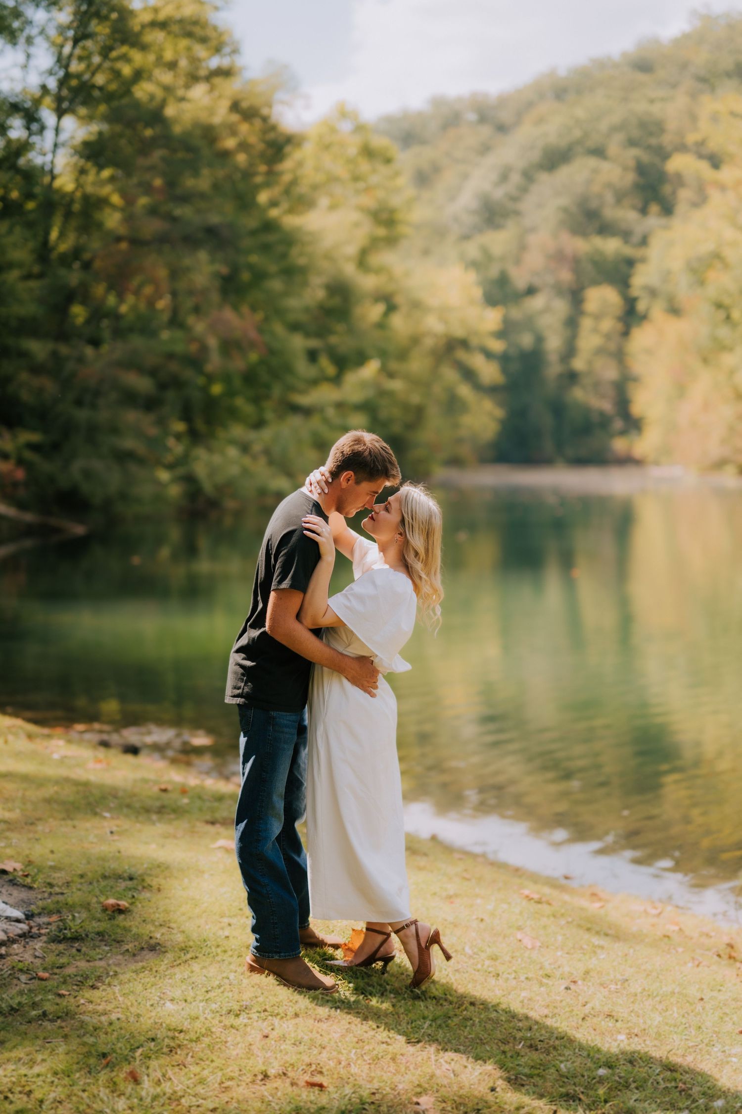 Couple embracing by serene lakeside with autumn forest reflections in water.