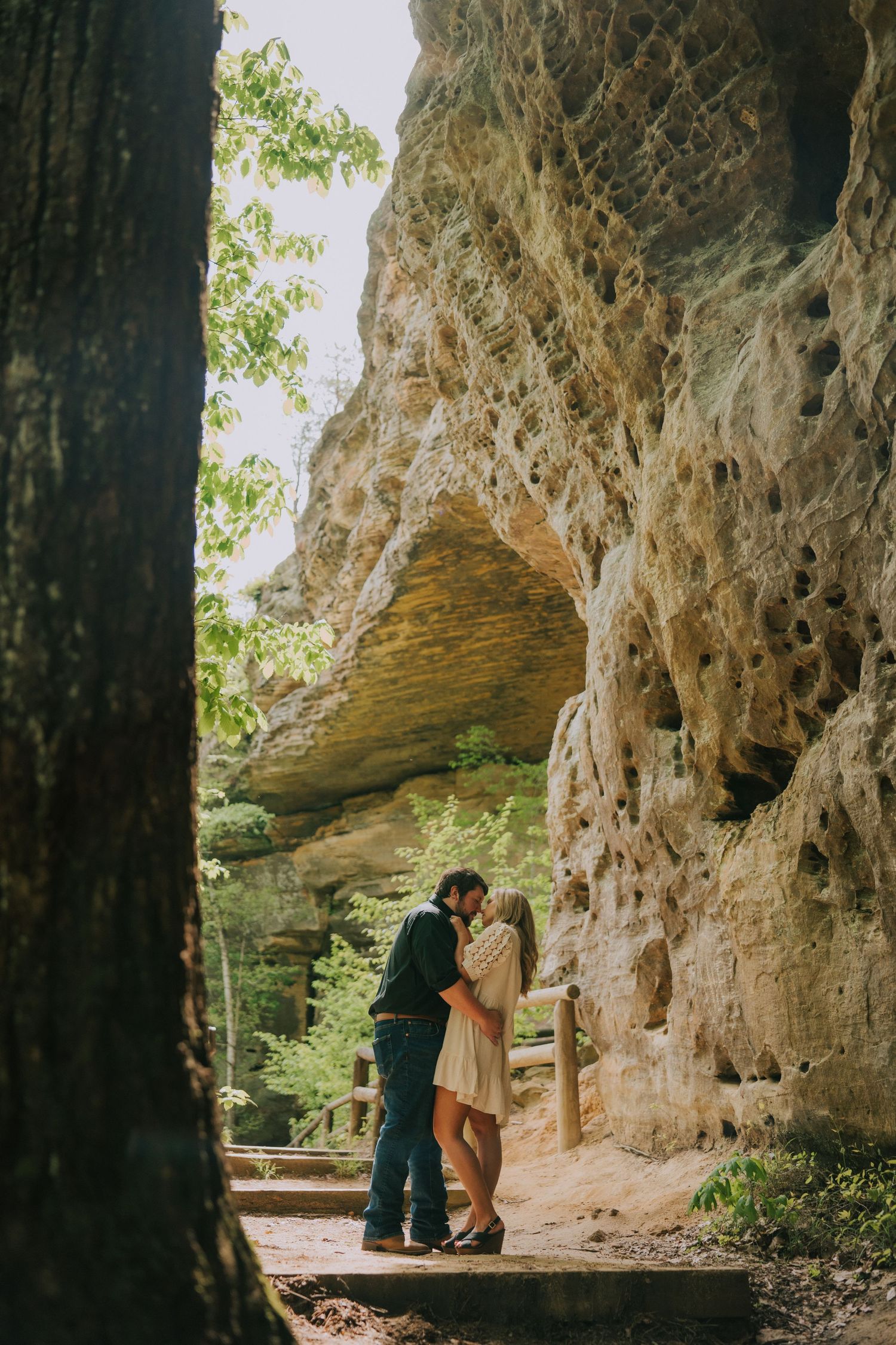Natural cave setting provides backdrop for romantic portrait beneath towering rock walls.