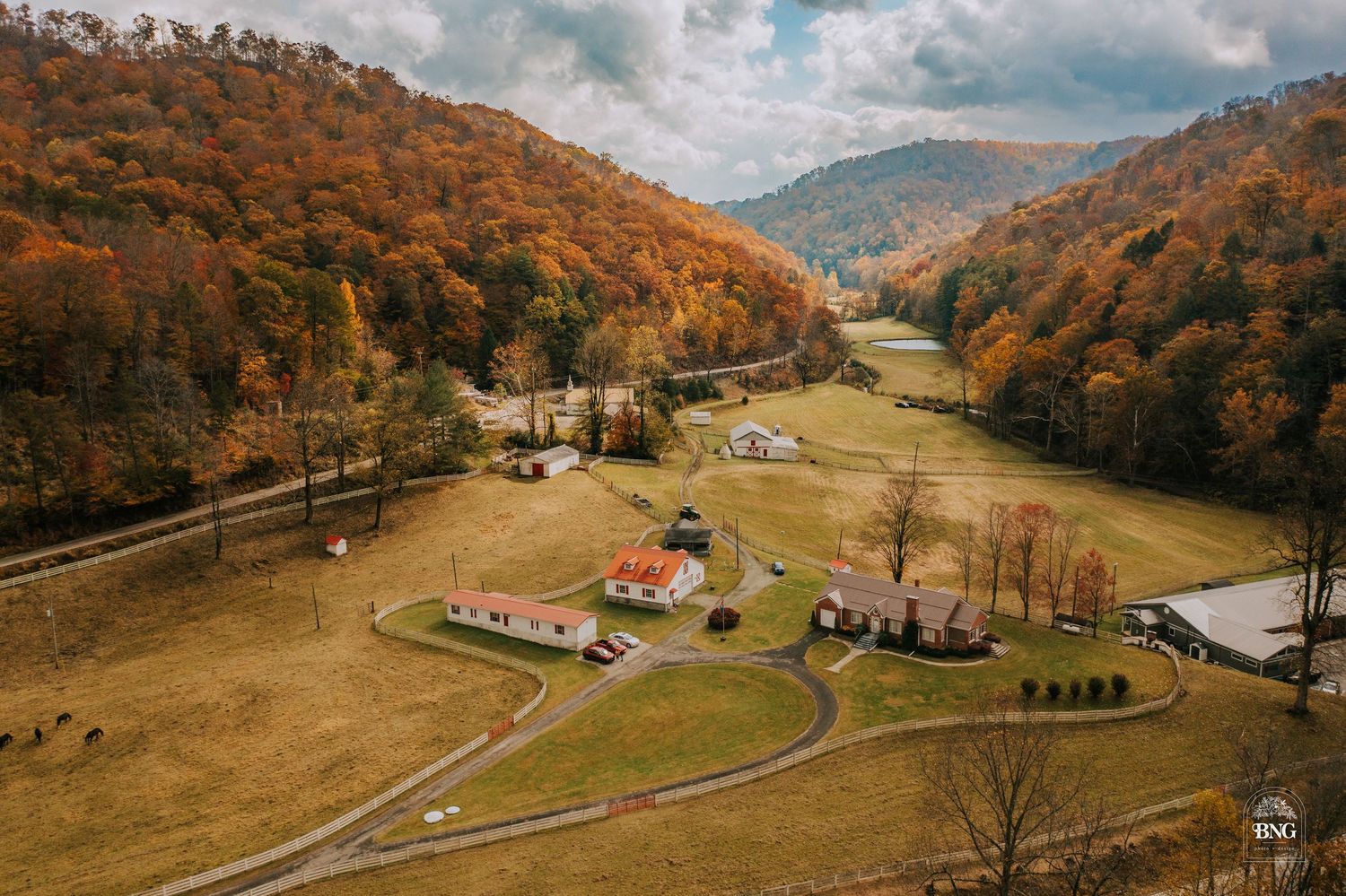 Aerial view of a valley with scattered buildings and winding roads nestled between autumn-colored mountains.