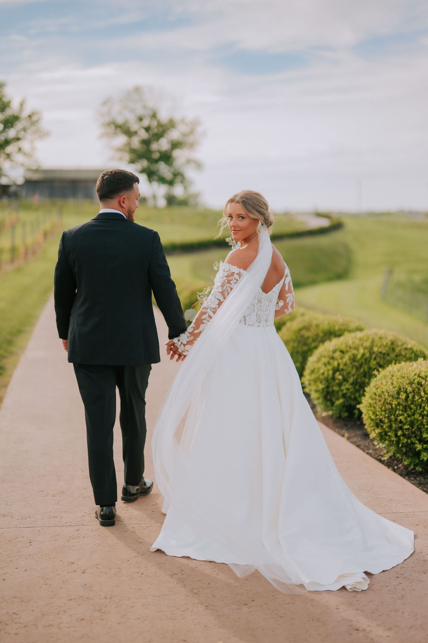 Newlyweds walking hand in hand along winding path through manicured garden.