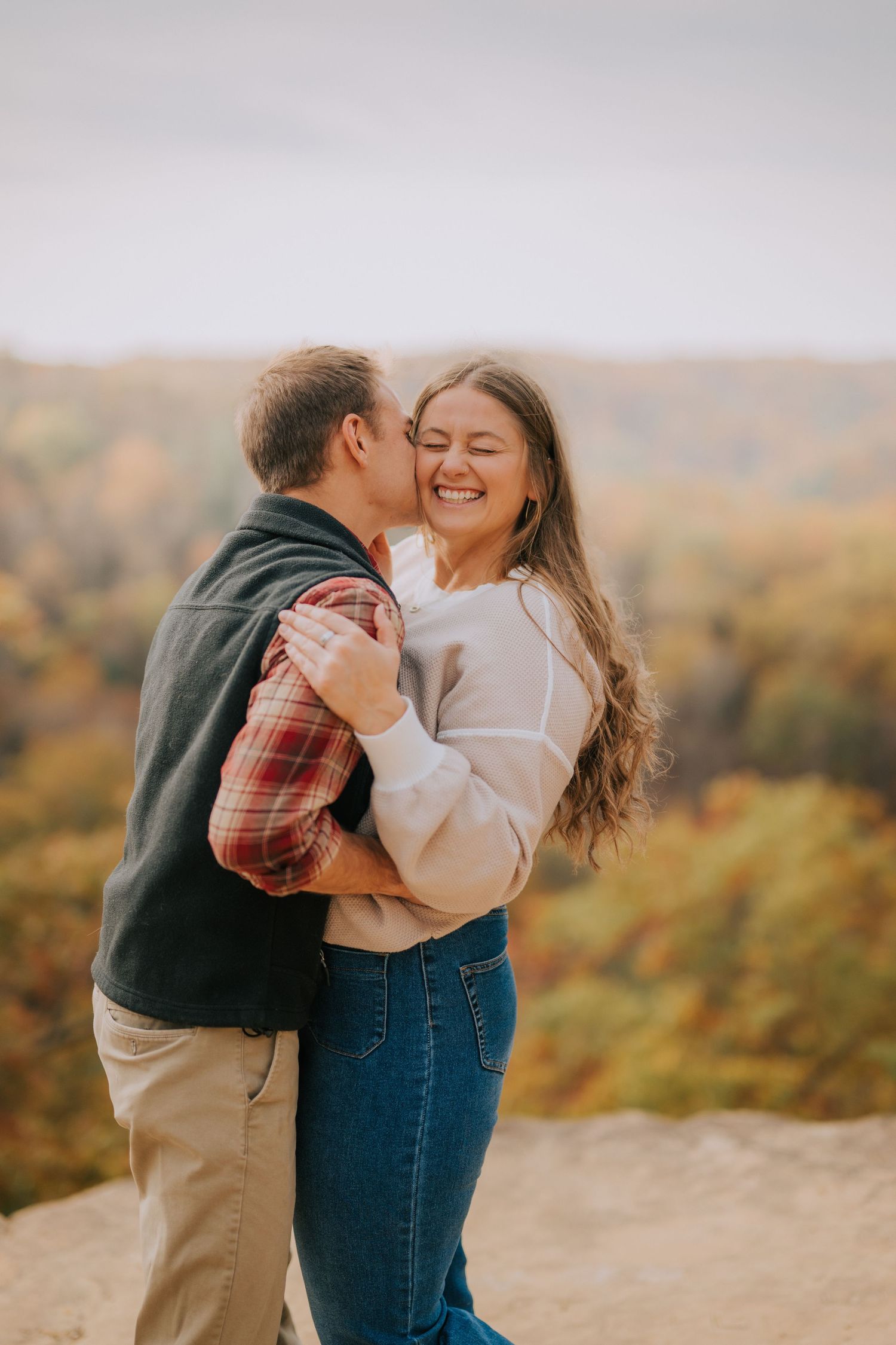A couple shares an intimate moment on a cliff overlooking autumn foliage.