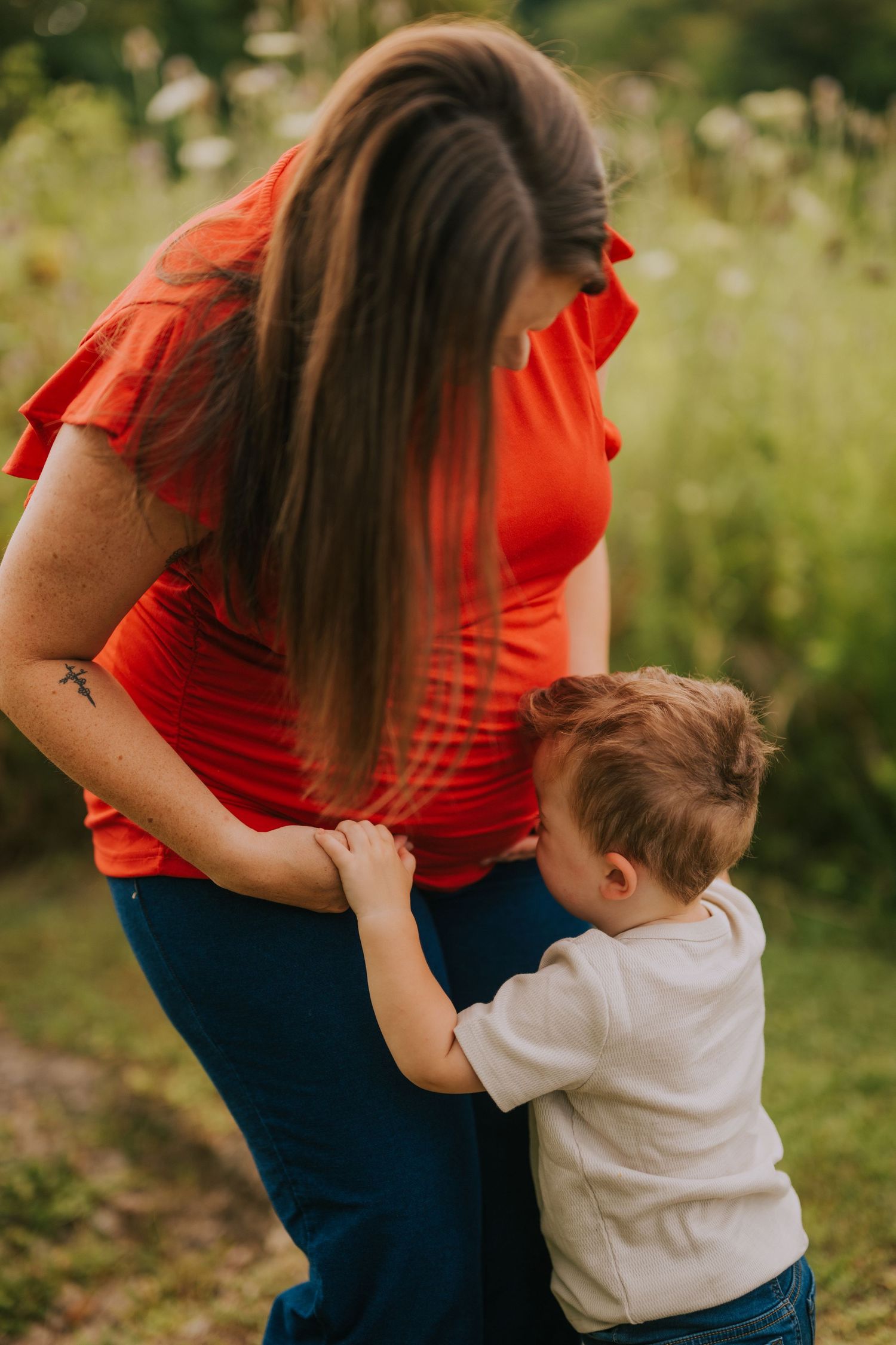 Mother in red shirt embracing child outdoors in natural setting.