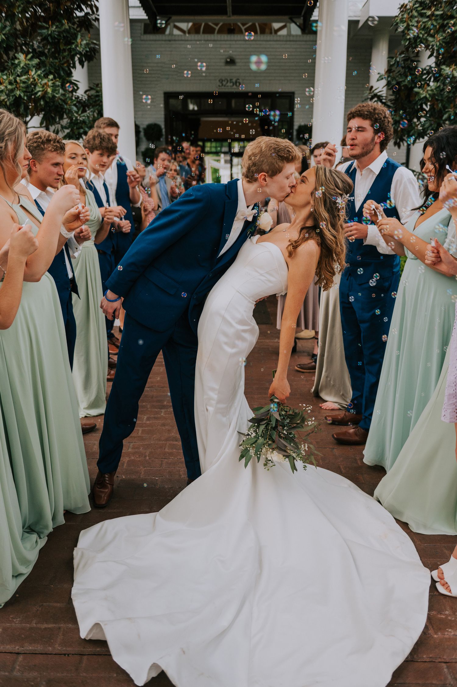 Wedding party dances together on a brick patio with bridesmaids in sage green dresses.