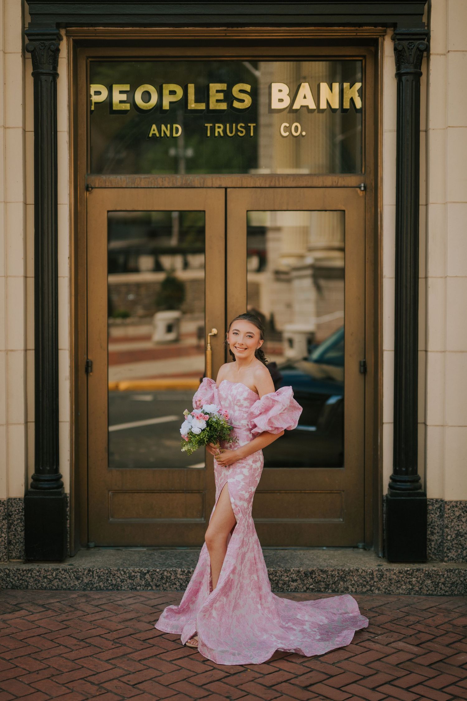 A flowing pink dress twirls in front of the historic Peoples Bank building.