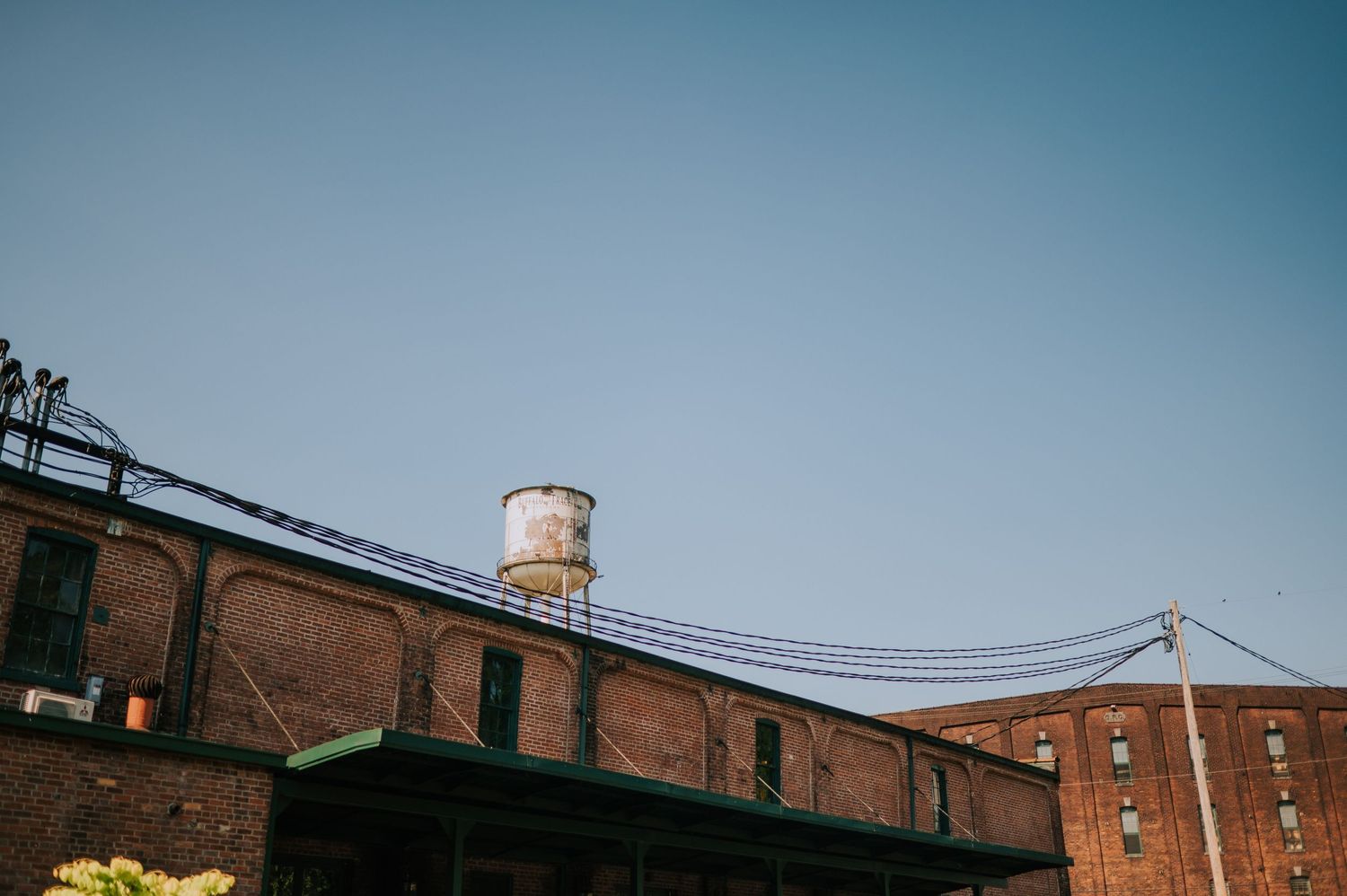 Industrial brick building with metal pipes and walkways against blue sky.