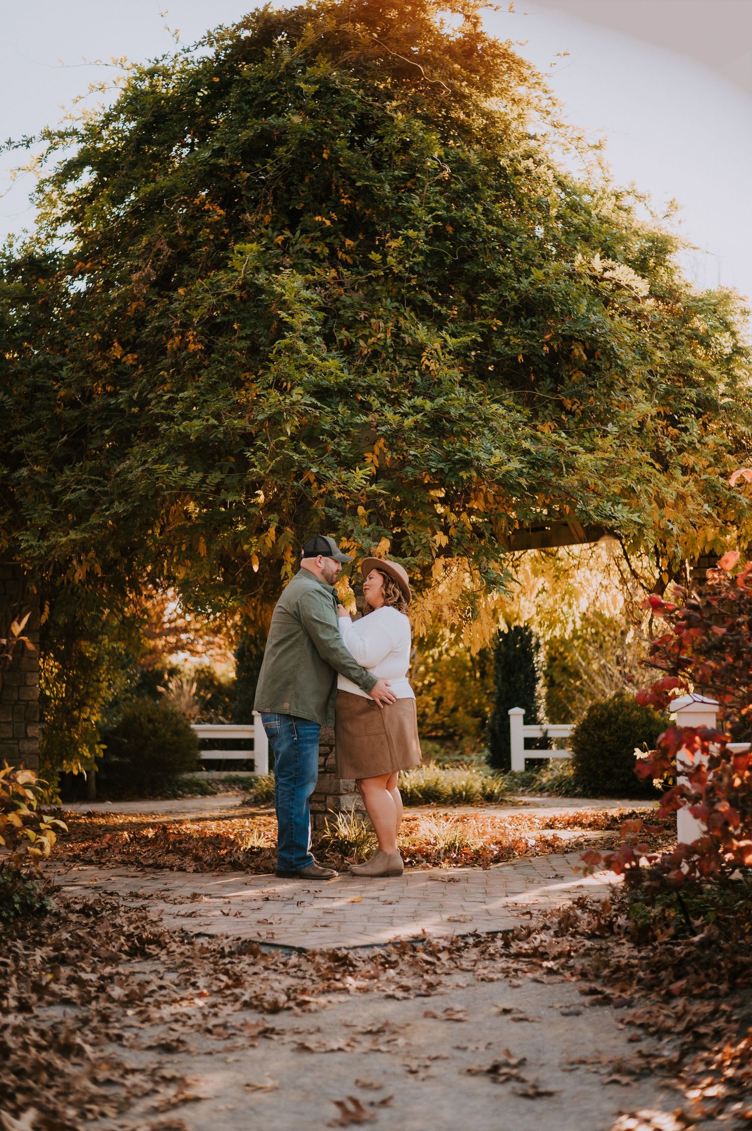 Autumn engagement photos with fallen leaves and golden sunlight filtering through trees.