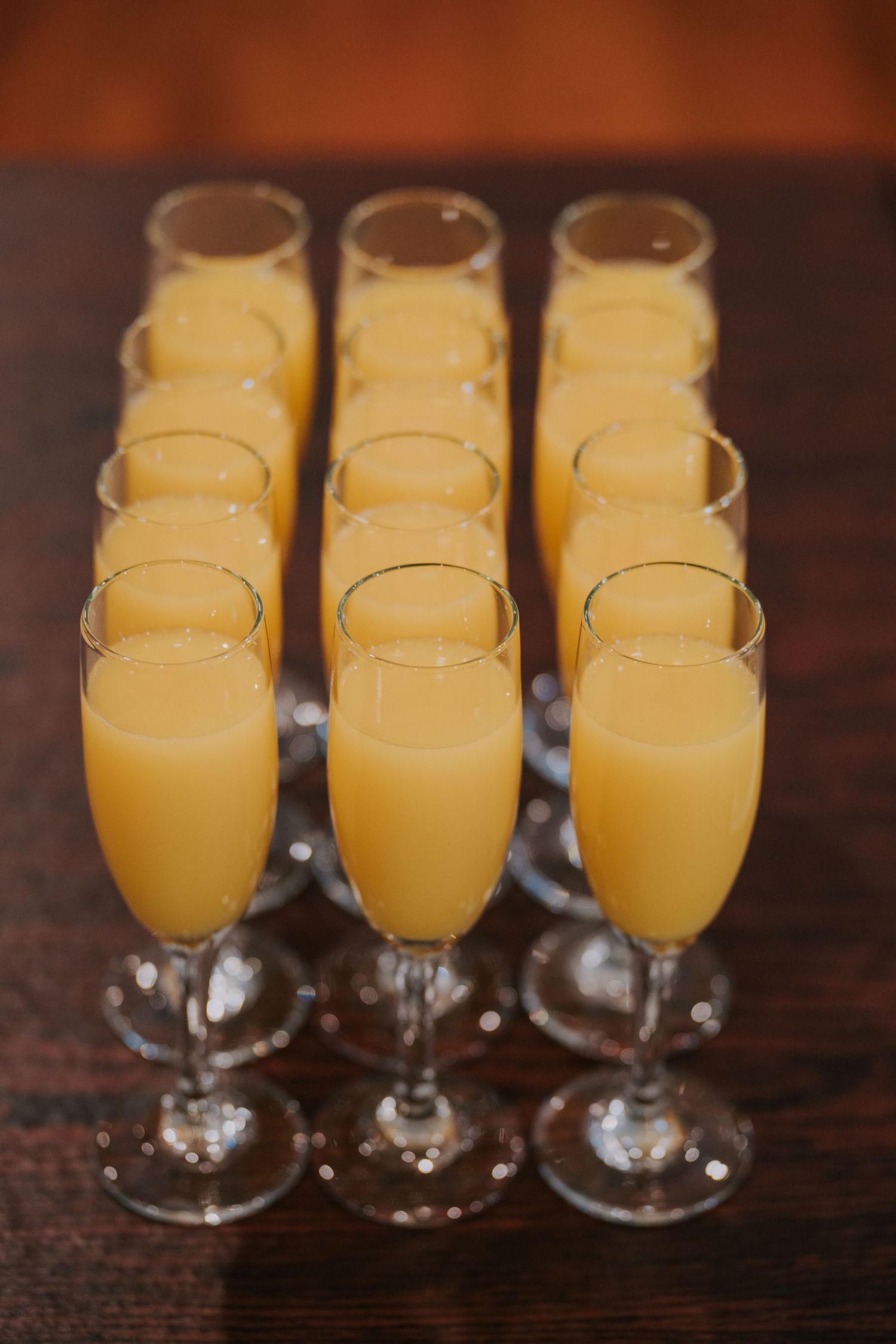 Rows of mimosa cocktails in champagne flutes arranged on a dark wooden surface.