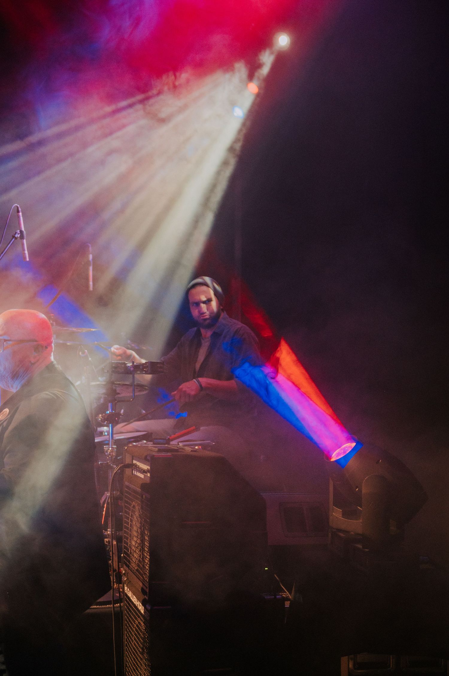 Performer playing keyboard under dramatic red and white spotlights with atmospheric fog.