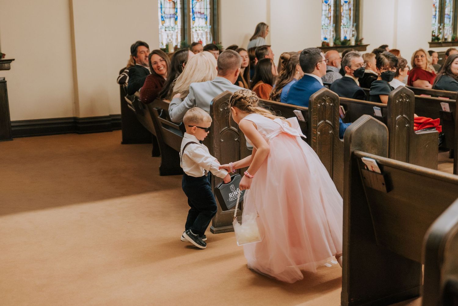A child interacts with someone wearing a pink ball gown in a church pew during what appears to be a special occasion.