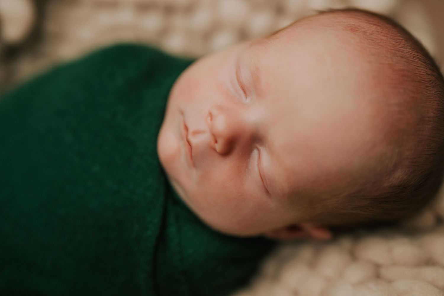Artistic close-up shots of a sleeping newborn on emerald green fabric.