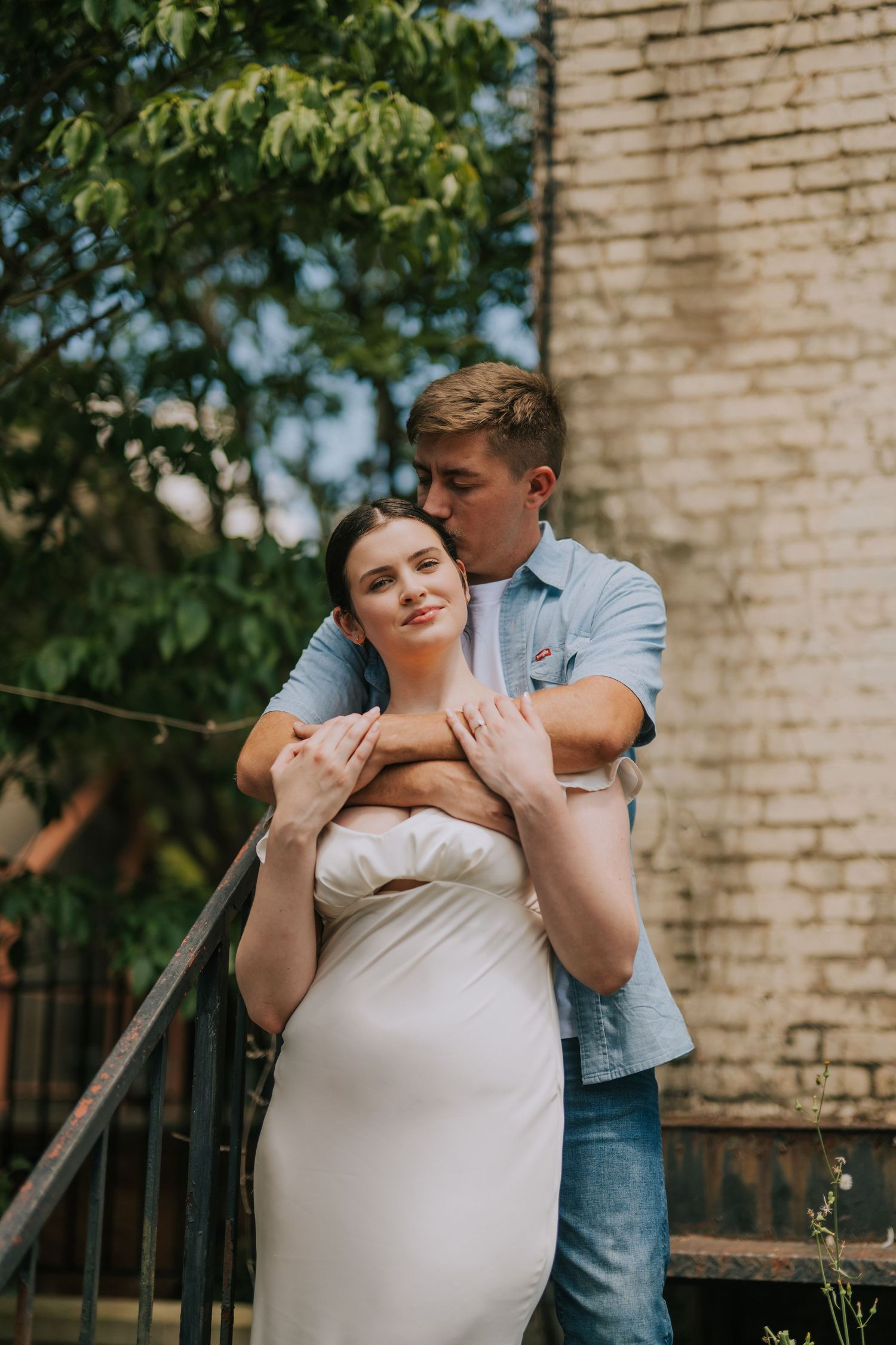 Romantic outdoor portrait session with couple embracing against a brick wall backdrop.