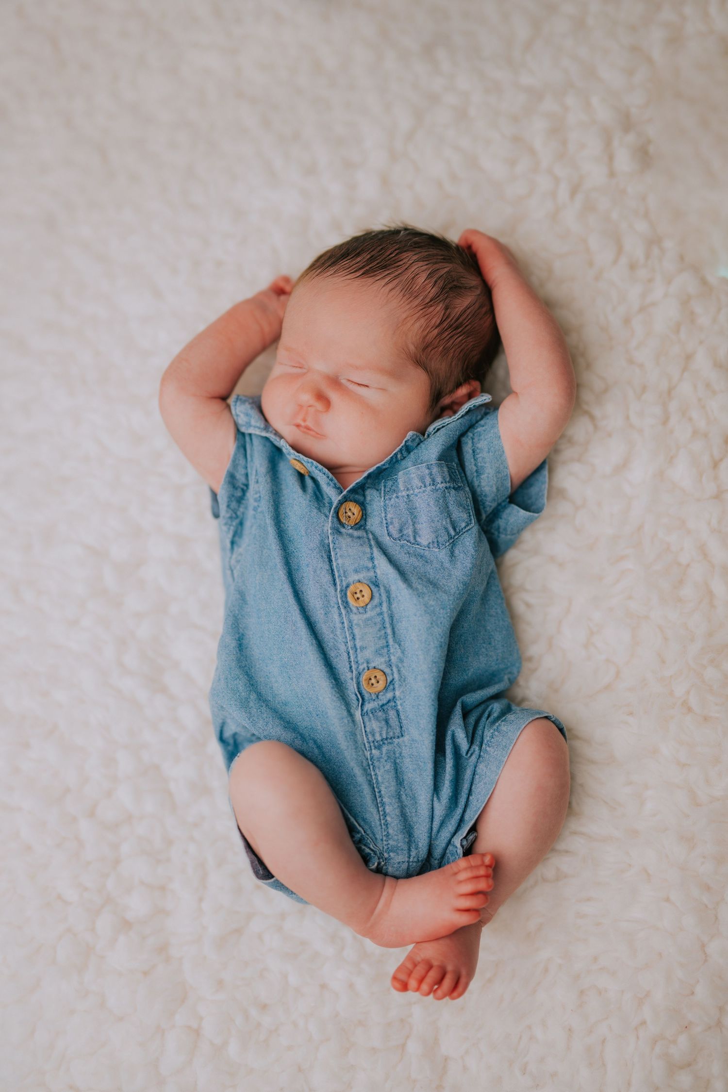 Sleeping newborn wearing chambray outfit on white textured background.
