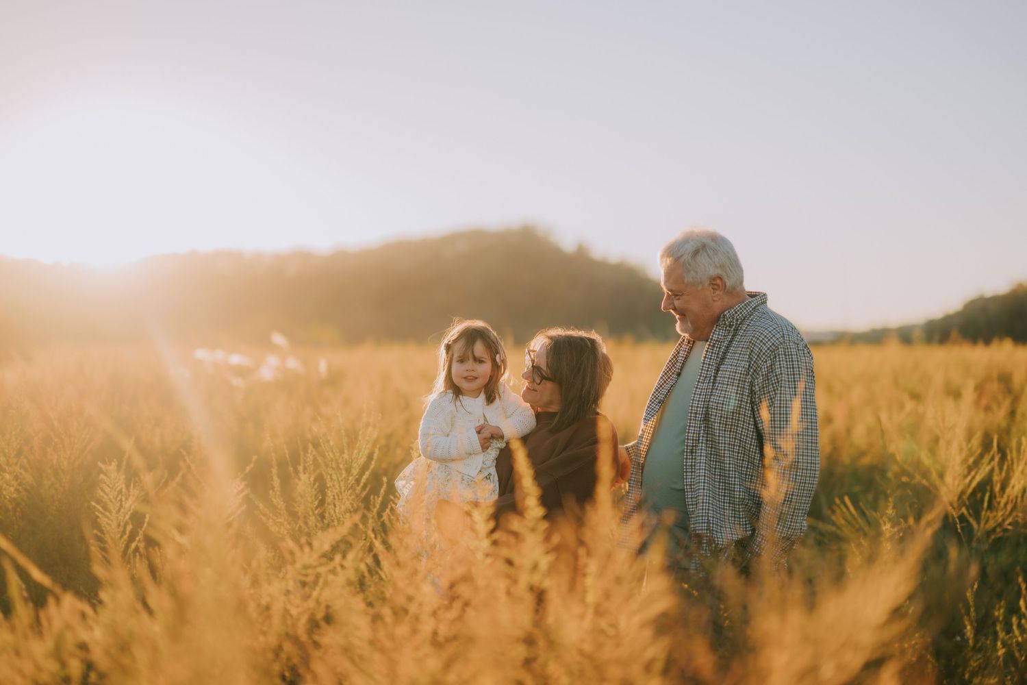 Three people share a tender moment together in a sunlit meadow.